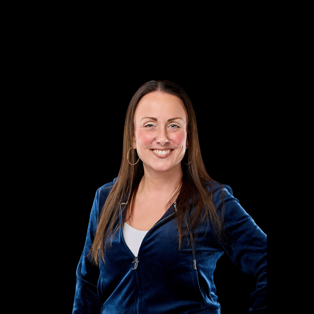 Joan Lenahan, Owner & Business Manager in a blue jacket is smiling in front of a black background.