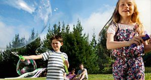 A boy and a girl are blowing soap bubbles in a park.