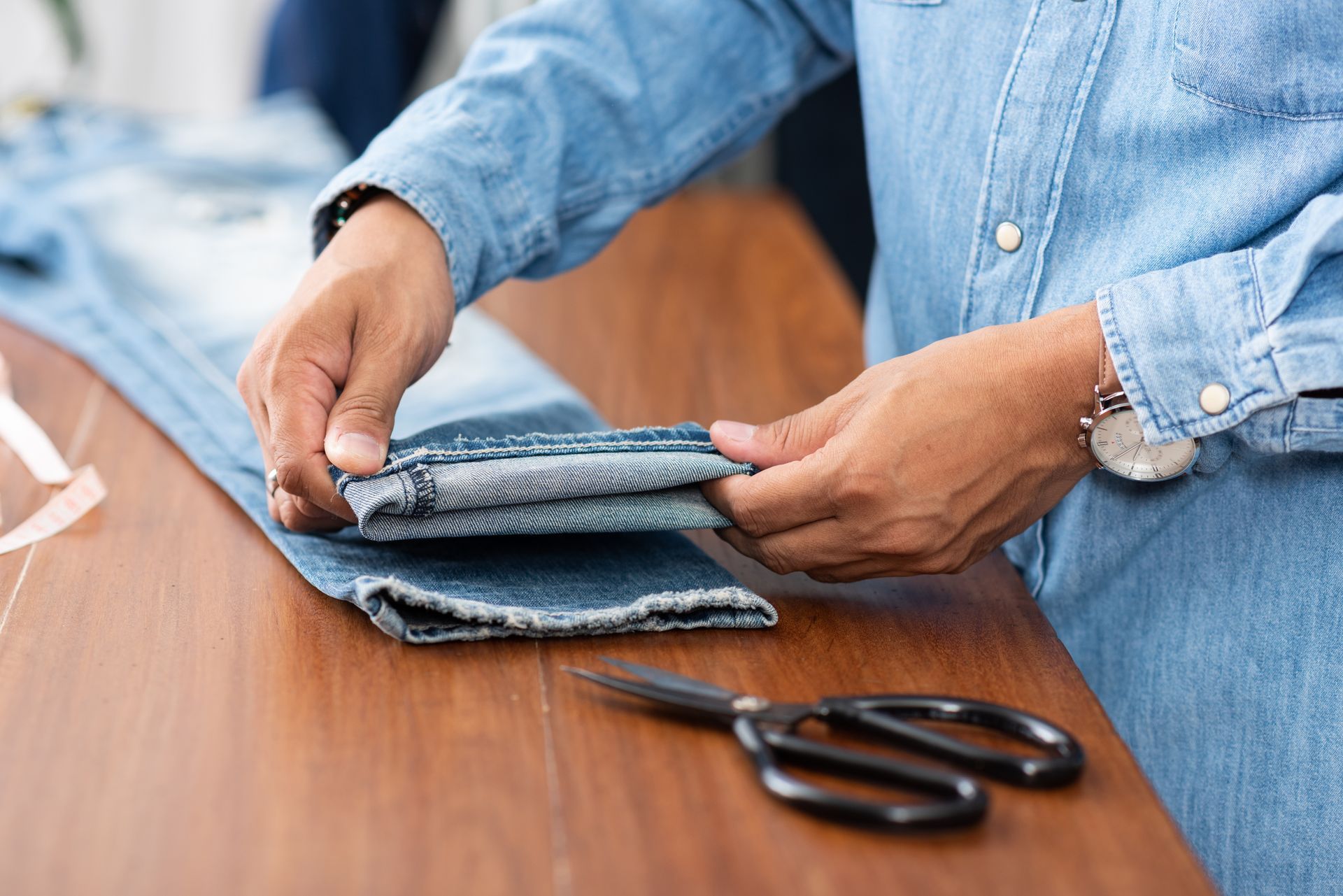 A person is cutting a pair of jeans with scissors on a wooden table.