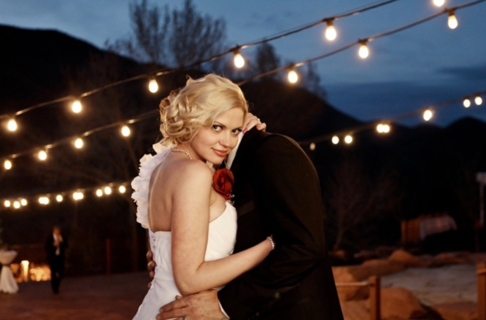 A woman in a white wedding dress is standing next to a table.