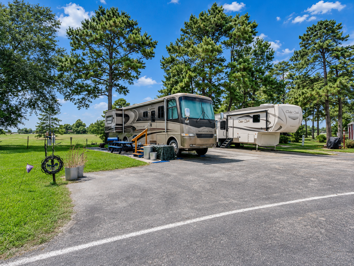 RV campsite with picnic table on a concrete pad, surrounded by trees and grass, with another RV nearby