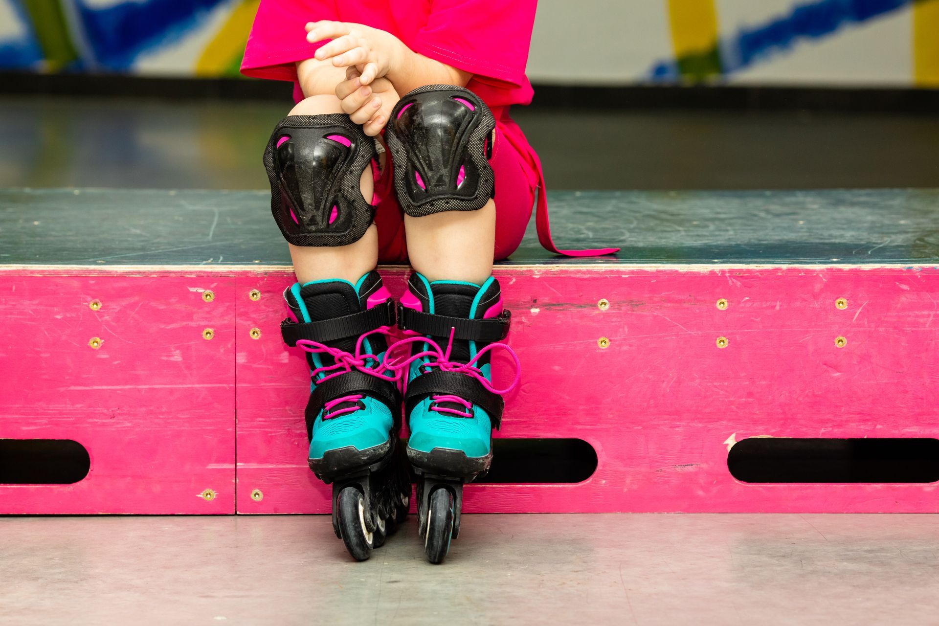 Child wearing black, pink, and teal roller skates sitting on a bright pink bench