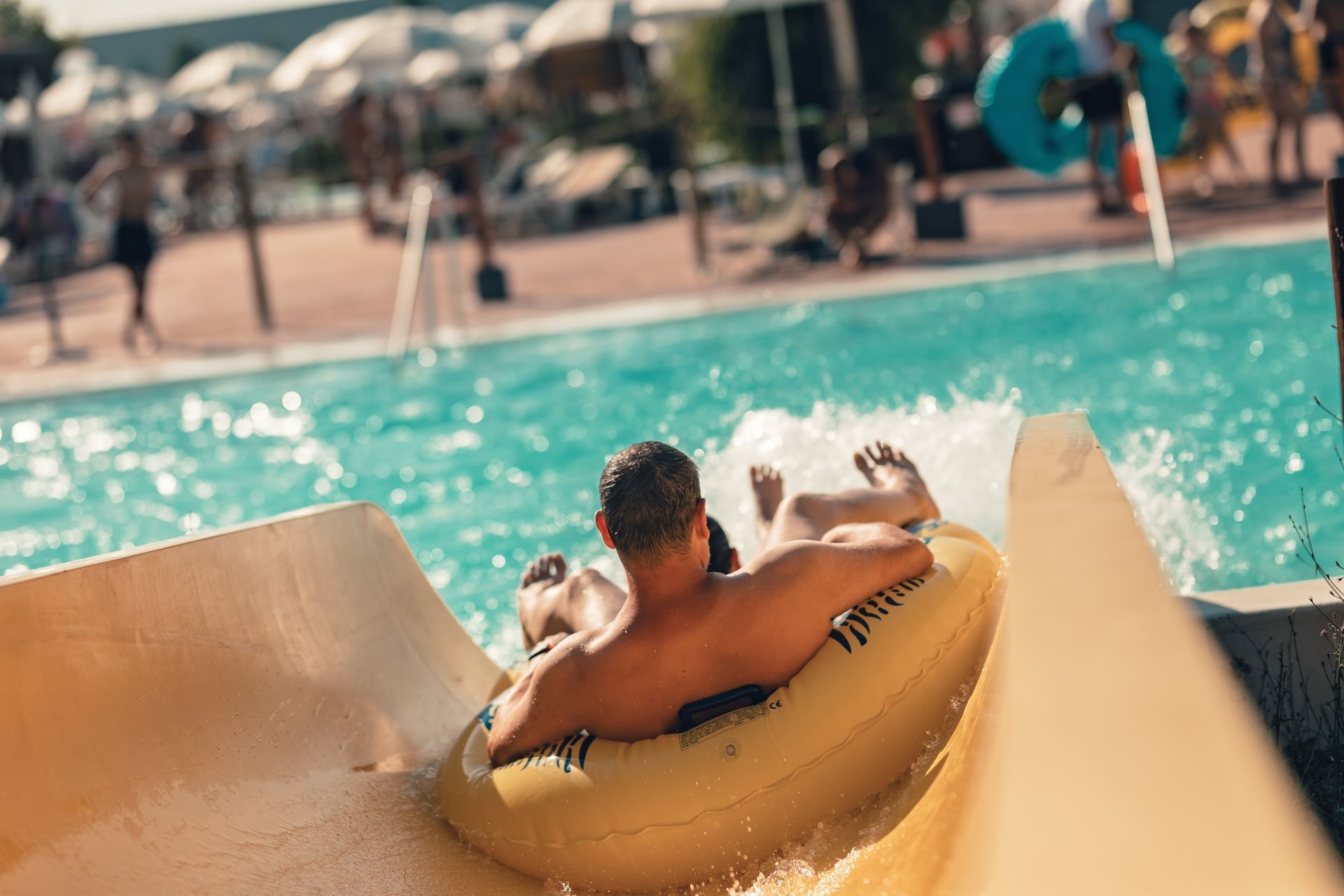 Person riding a yellow pool slide into a turquoise swimming pool