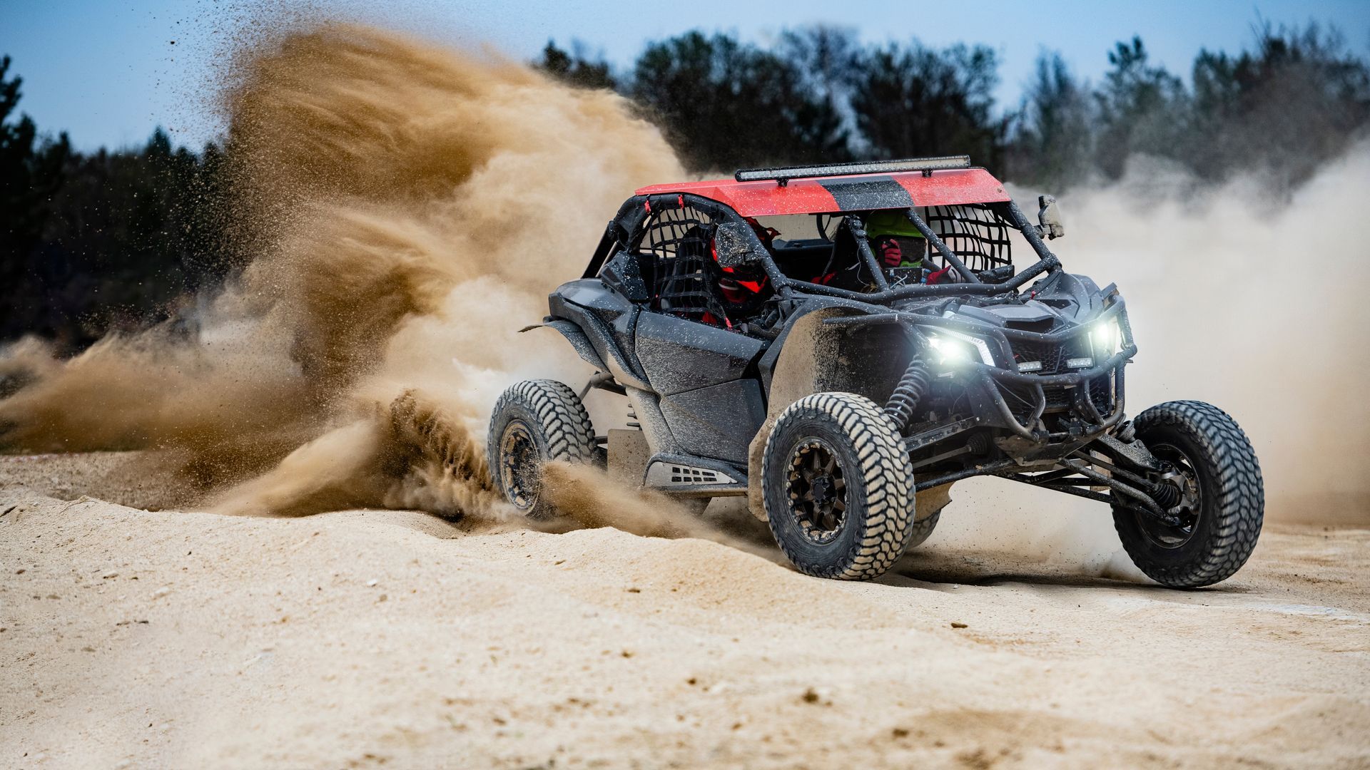 Off-road buggy racing through sand, kicking up a large dust cloud in a desert setting
