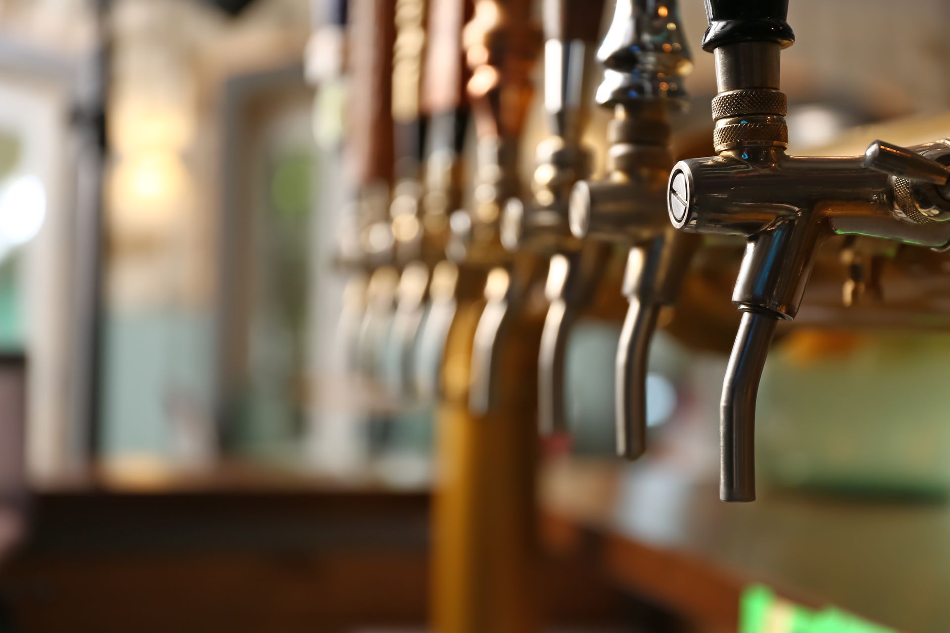 Row of beer taps in a softly lit bar, with metal spouts in the foreground