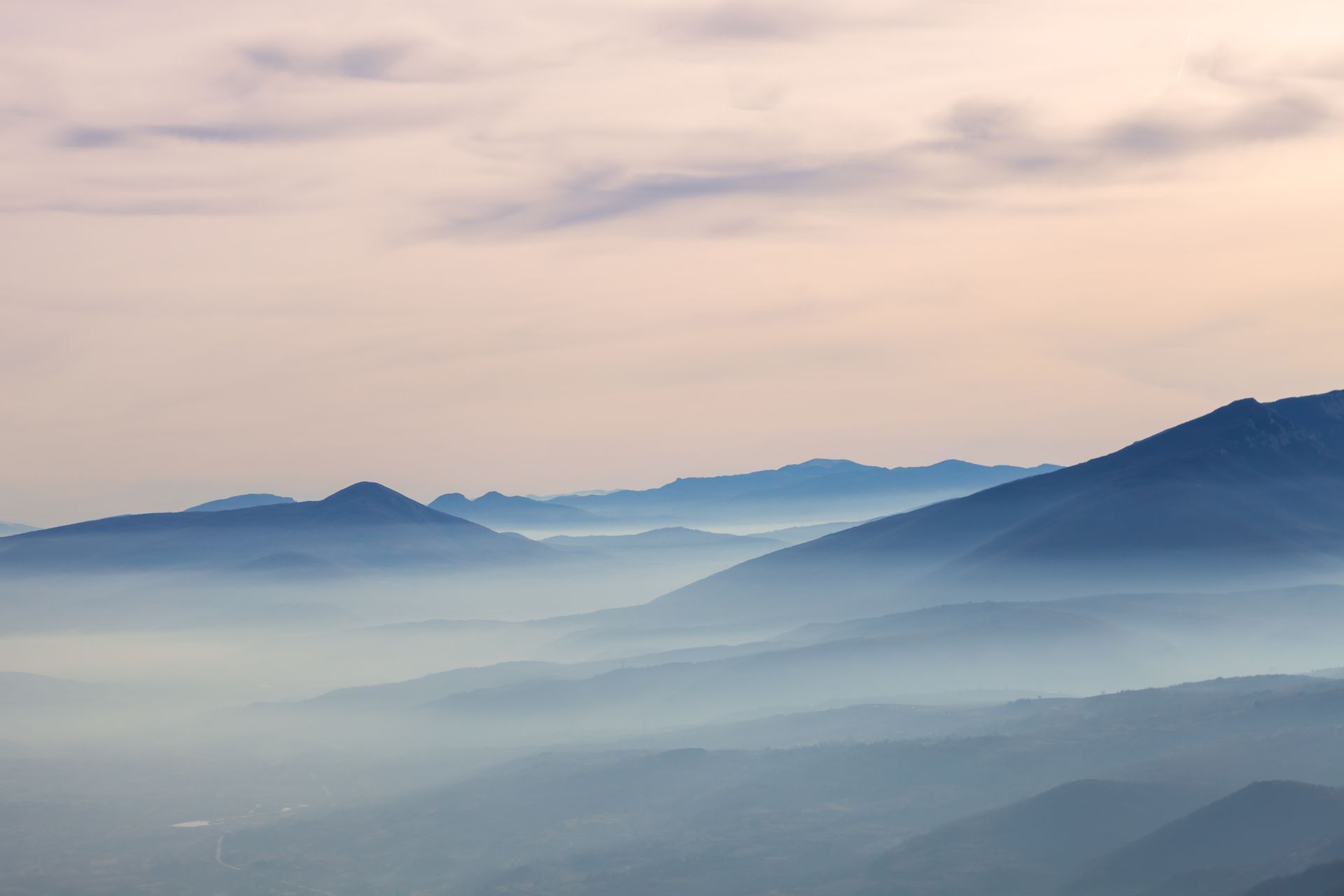 Misty blue mountain ridges under a soft pink sunrise sky