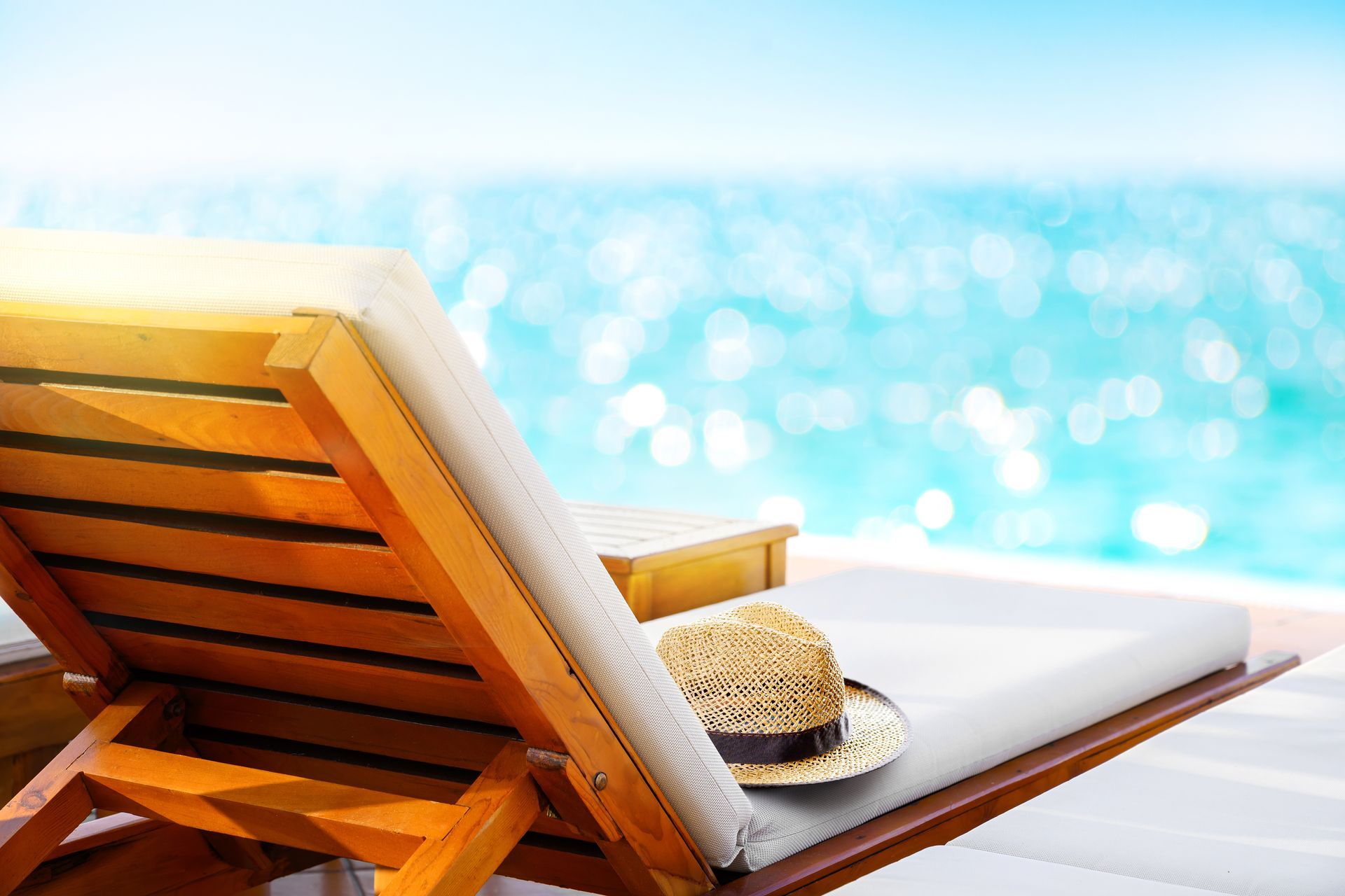 Beach lounge chair with a straw hat, facing a bright blue ocean