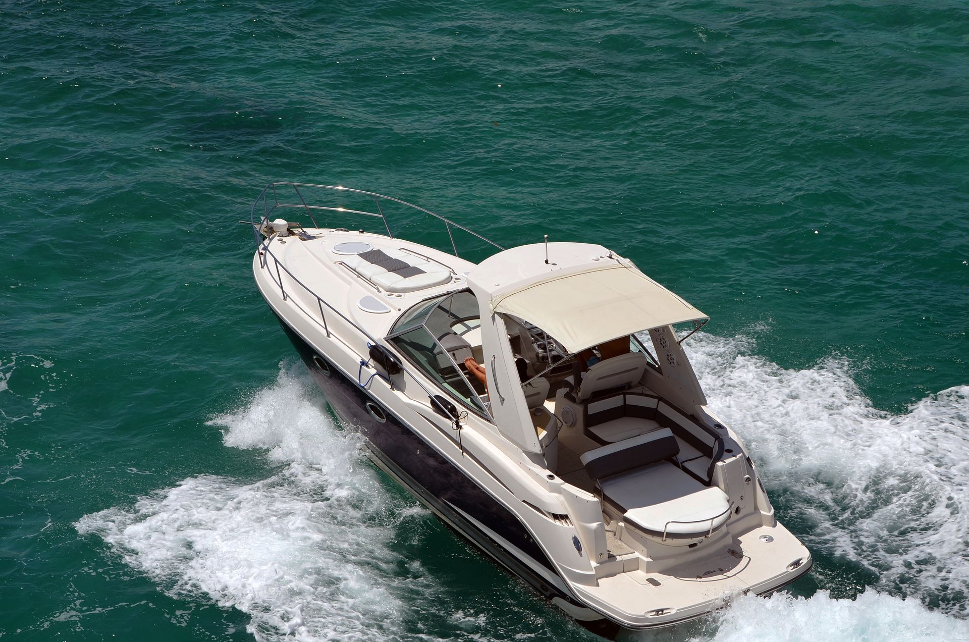 White motor yacht speeding across green water, leaving a foamy wake