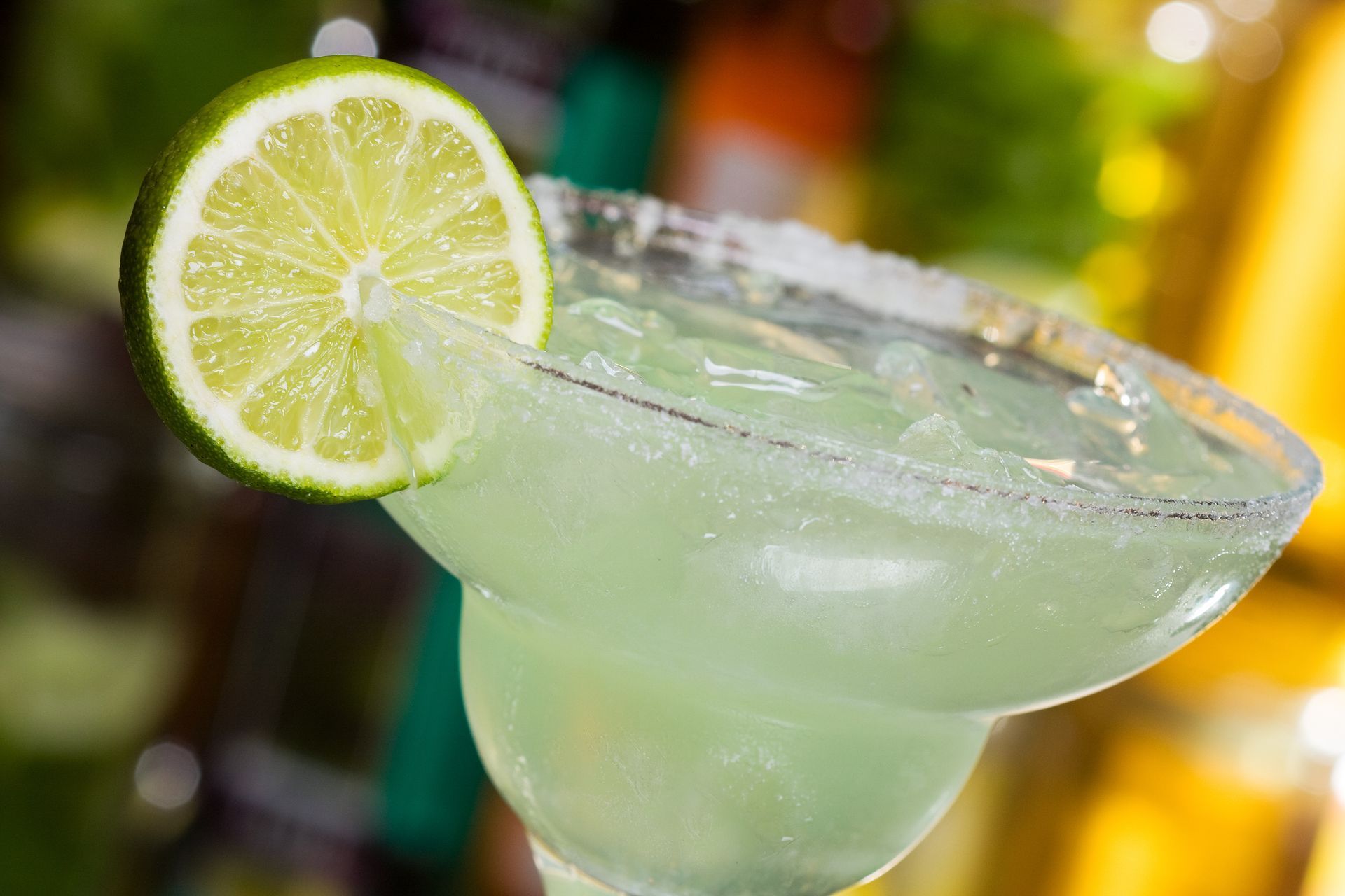 Lime margarita in a salt-rimmed glass with a lime slice, on a blurred bar counter