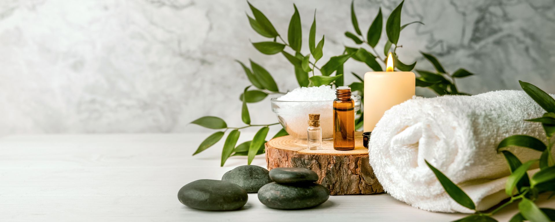 Spa still life with candles, stones, towels, and green leaves on a white tabletop