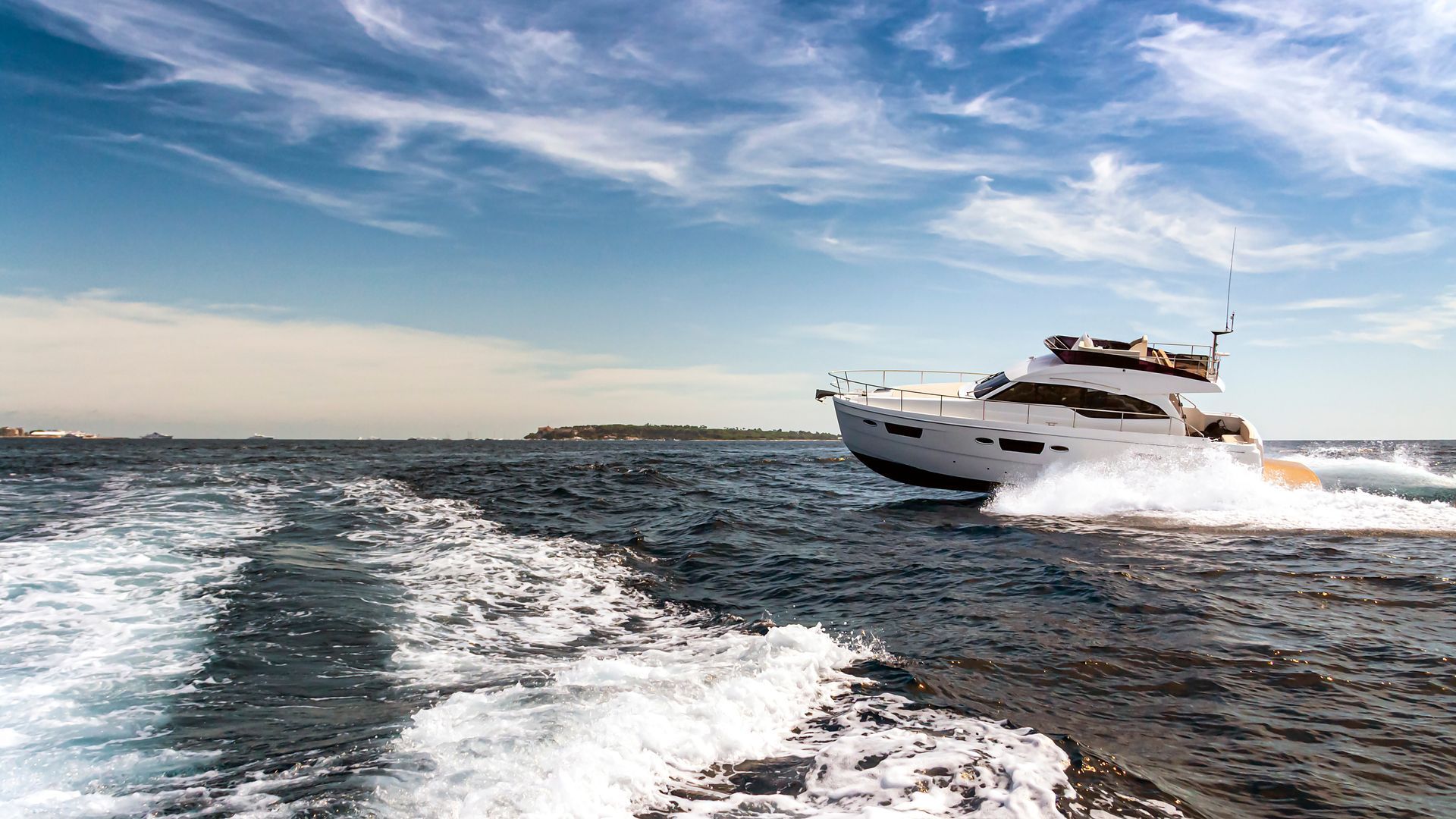 White yacht speeding across choppy water, leaving a foamy wake under a blue sky.