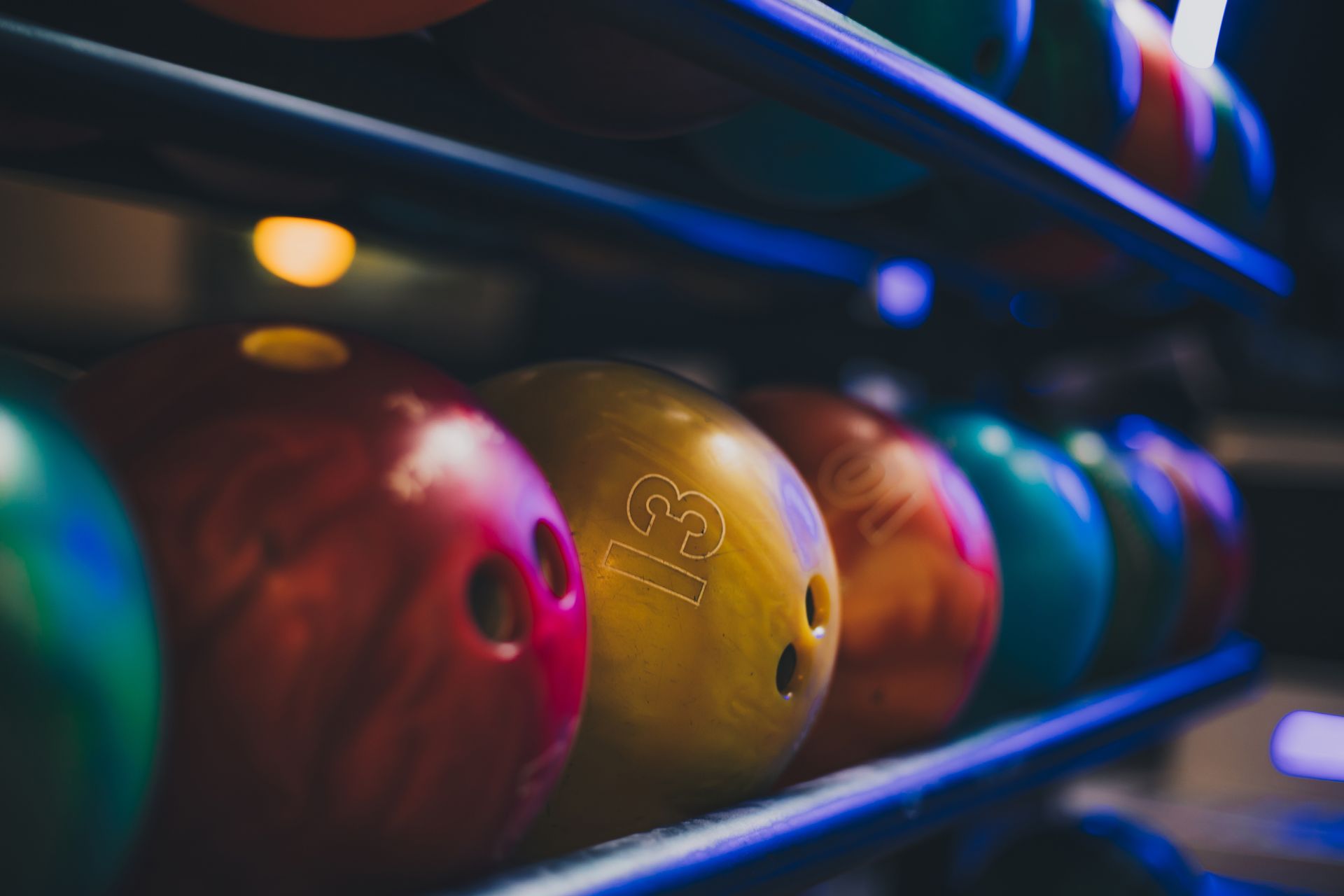 Colorful bowling balls lined up on a rack in a dim bowling alley