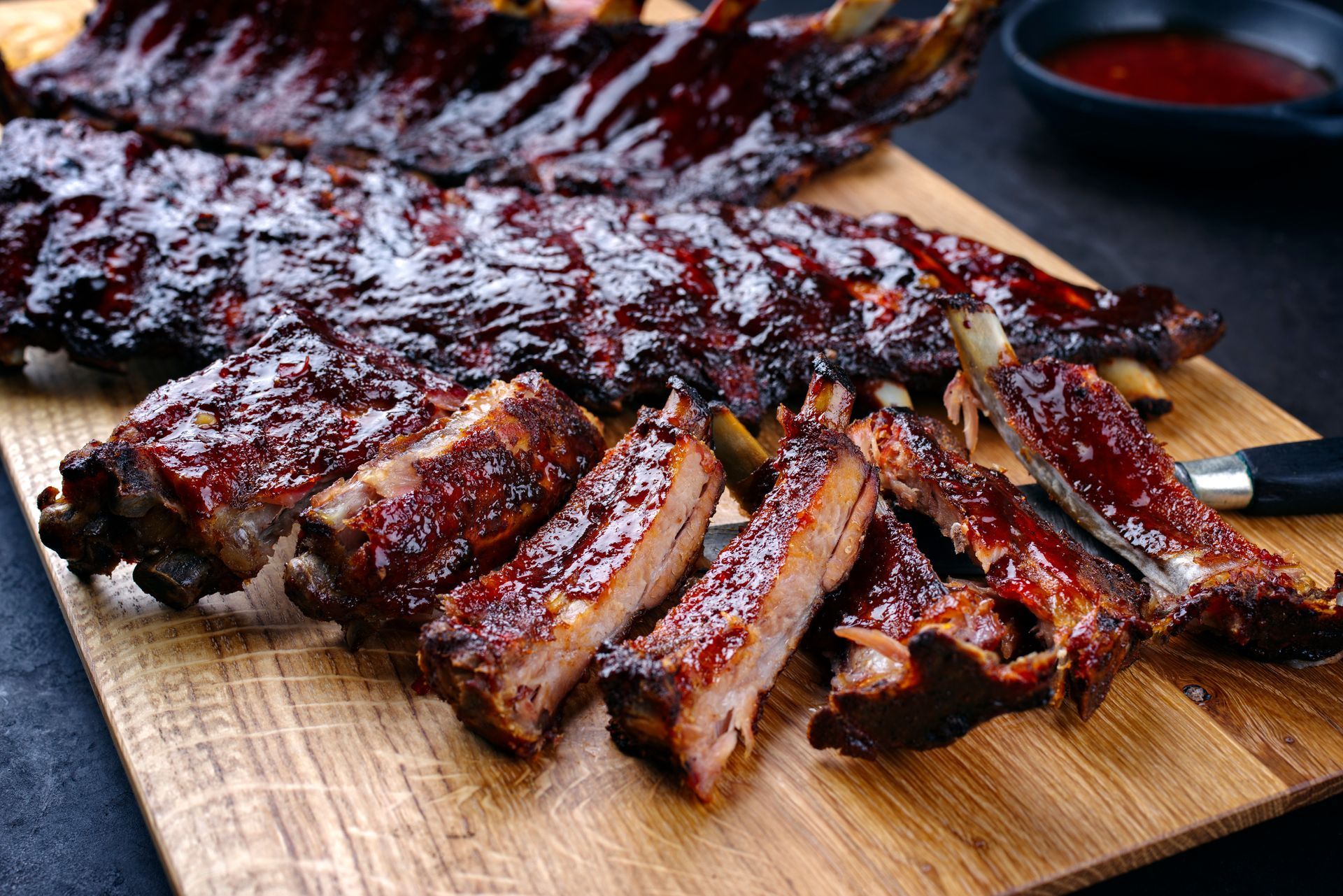 Glazed barbecued ribs sliced on a wooden cutting board with dipping sauce nearby
