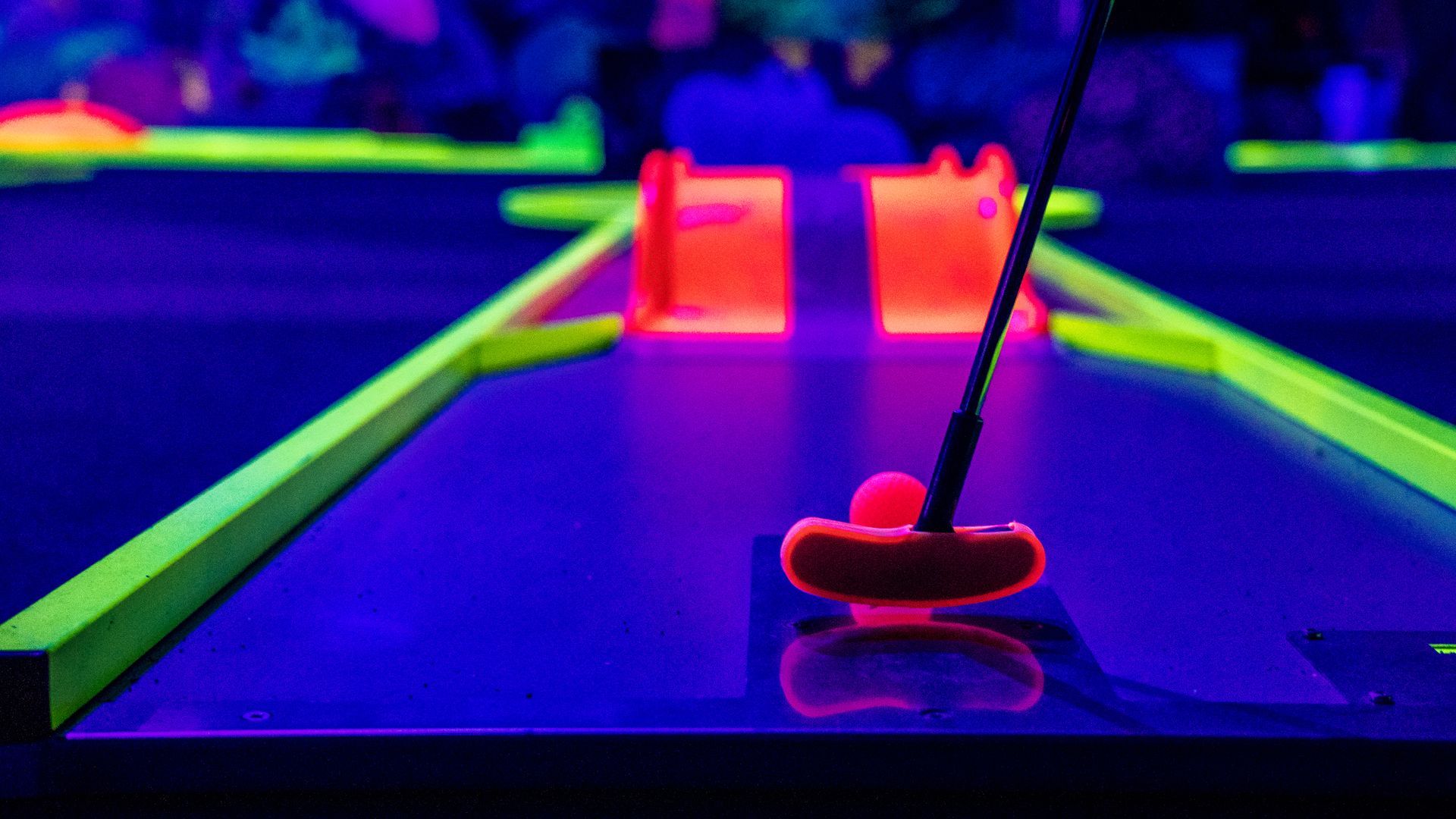 Neon-lit miniature golf hole with a red putter and glowing pink obstacles on a blue-green course
