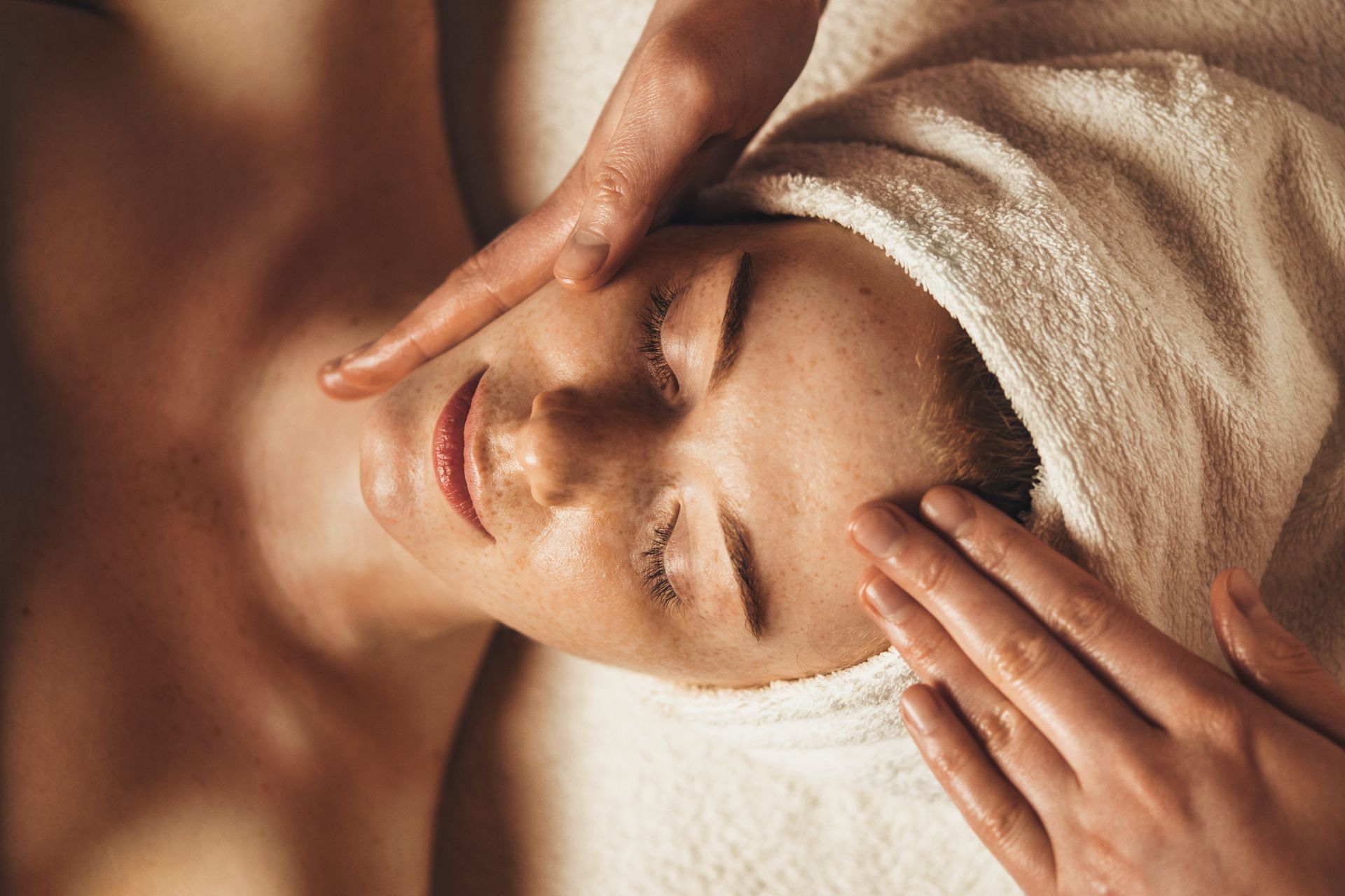 Person receiving a facial massage with a towel wrapped around their head