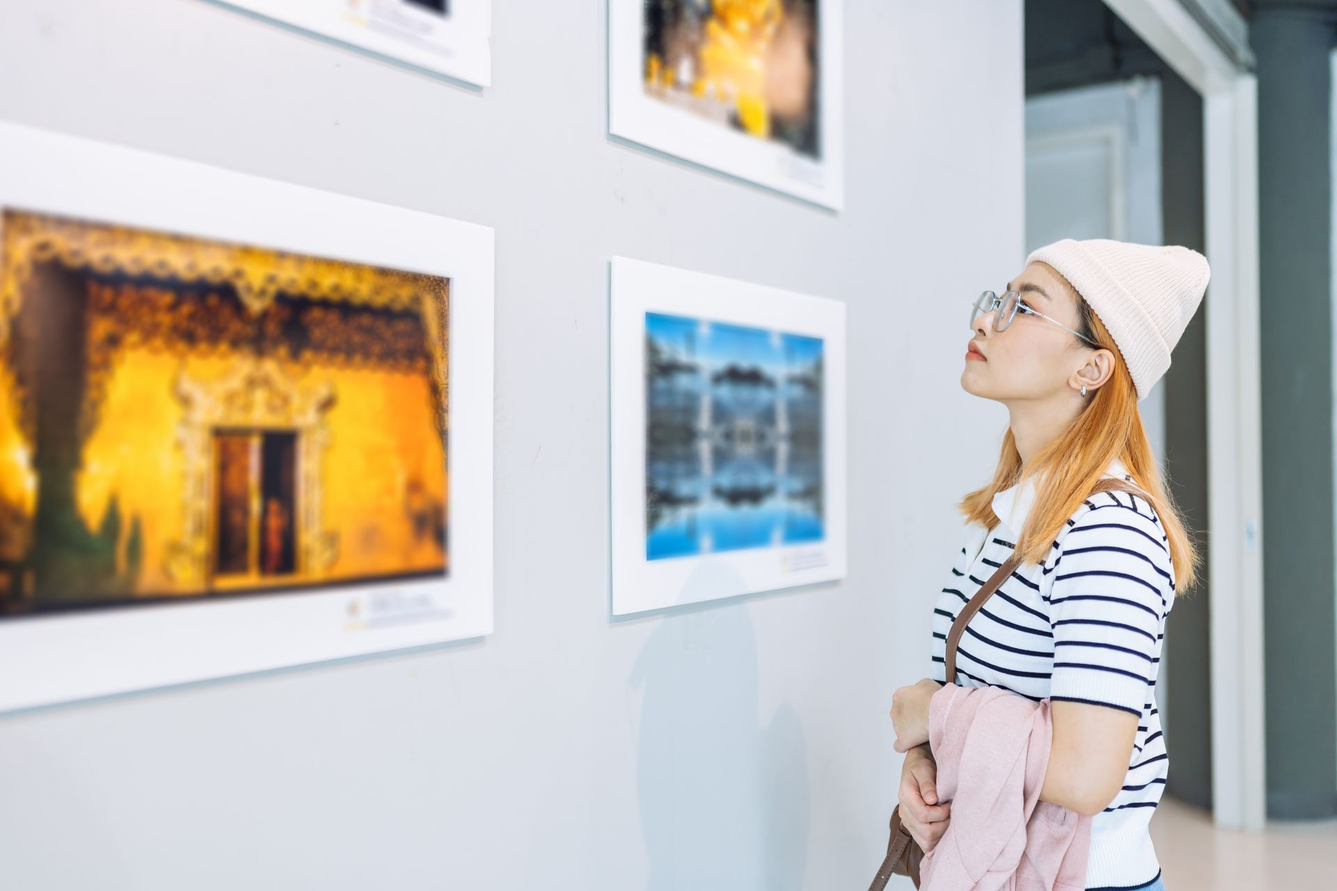 Woman in a beanie viewing framed photos in a bright gallery.