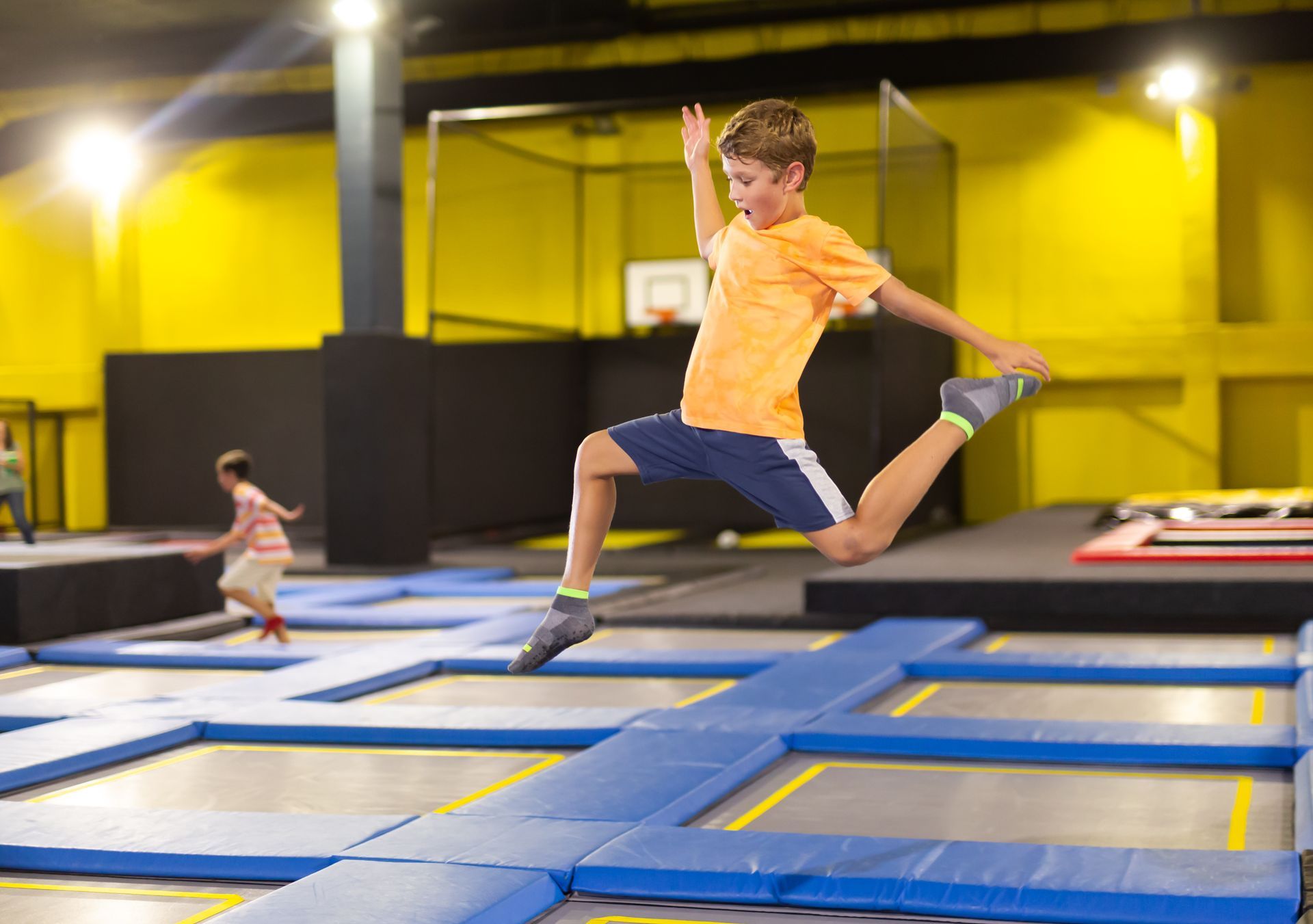 Boy jumping on a trampoline park, midair over blue mats with yellow walls in the background