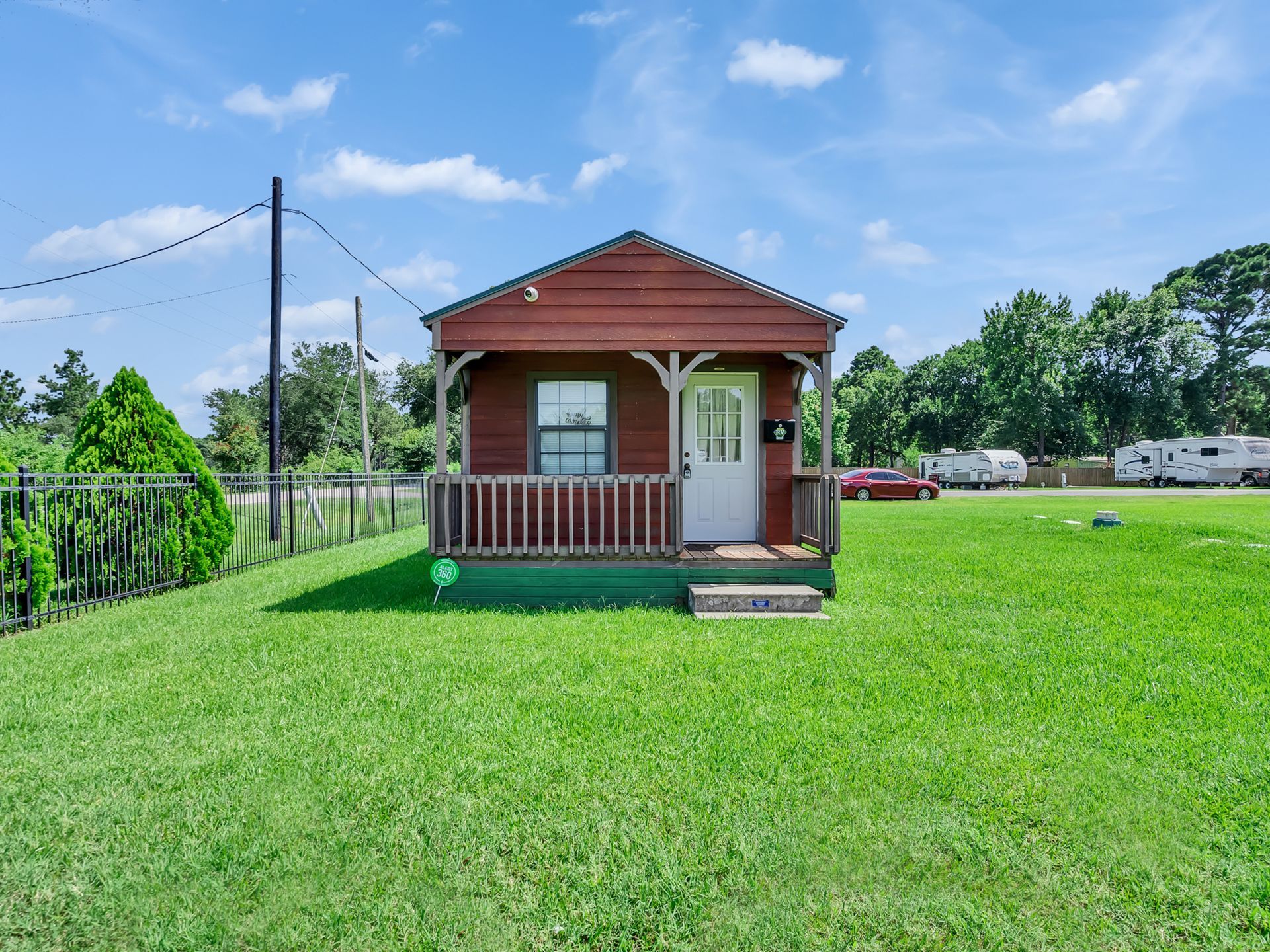 Small red cabin with porch in a grassy field under a blue sky