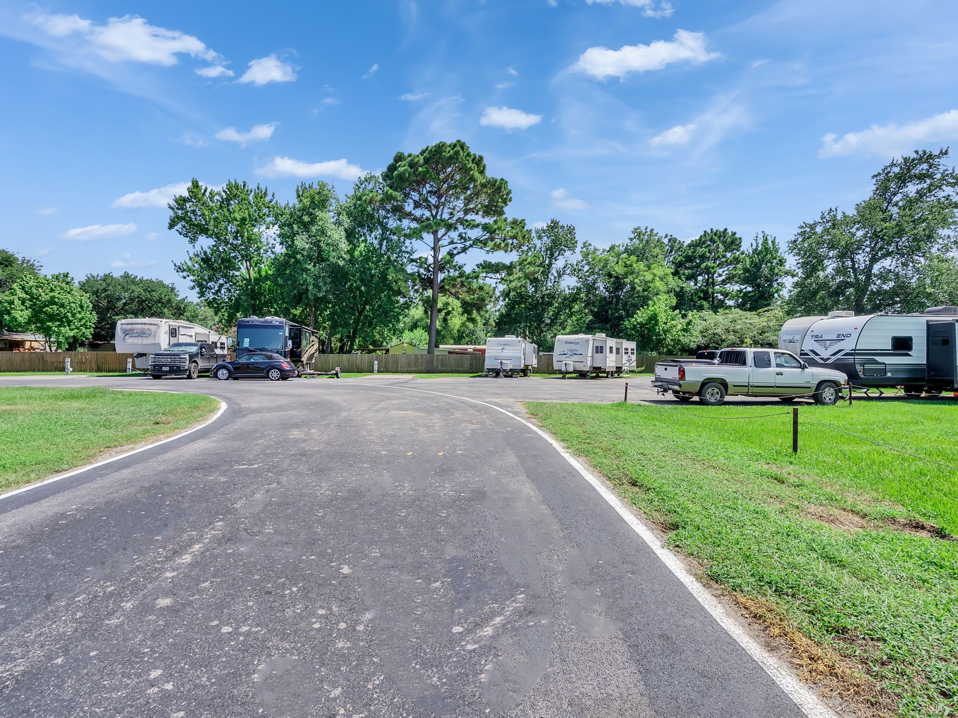 RV park with parked trucks and trailers along a paved road under a blue sky