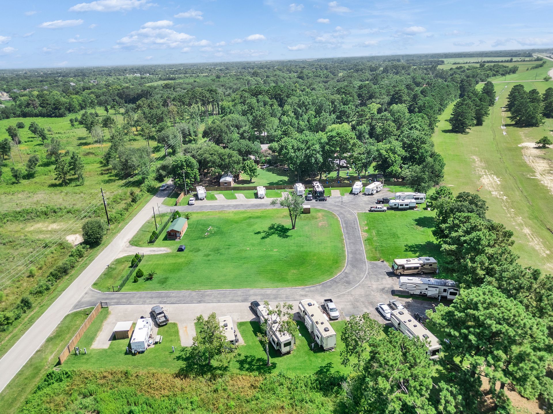 Aerial view of a rural campground with cabins, parked RVs, and green fields surrounded by trees.