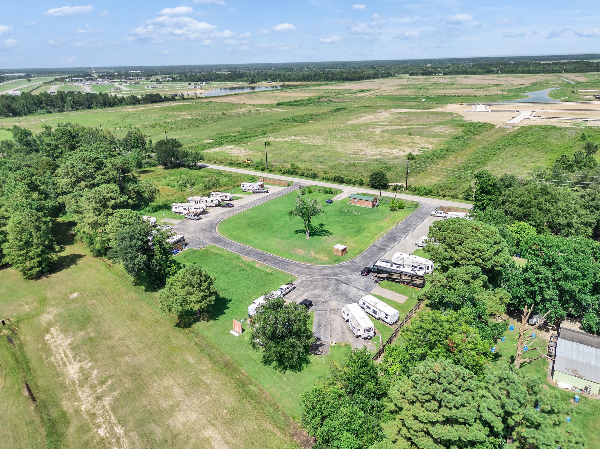 Aerial view of a circular paved driveway surrounded by trees and open fields under a bright sky