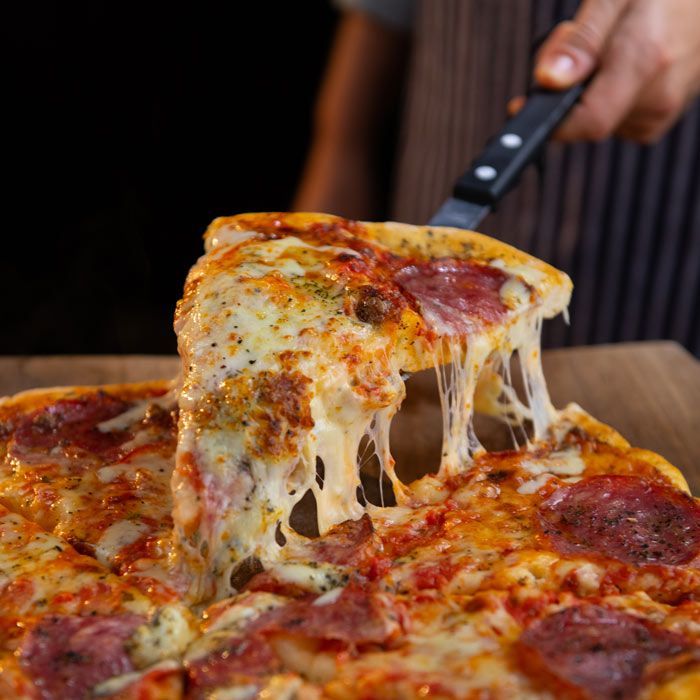 Cheesy pepperoni pizza slice being lifted from a pan, with melted cheese stretching