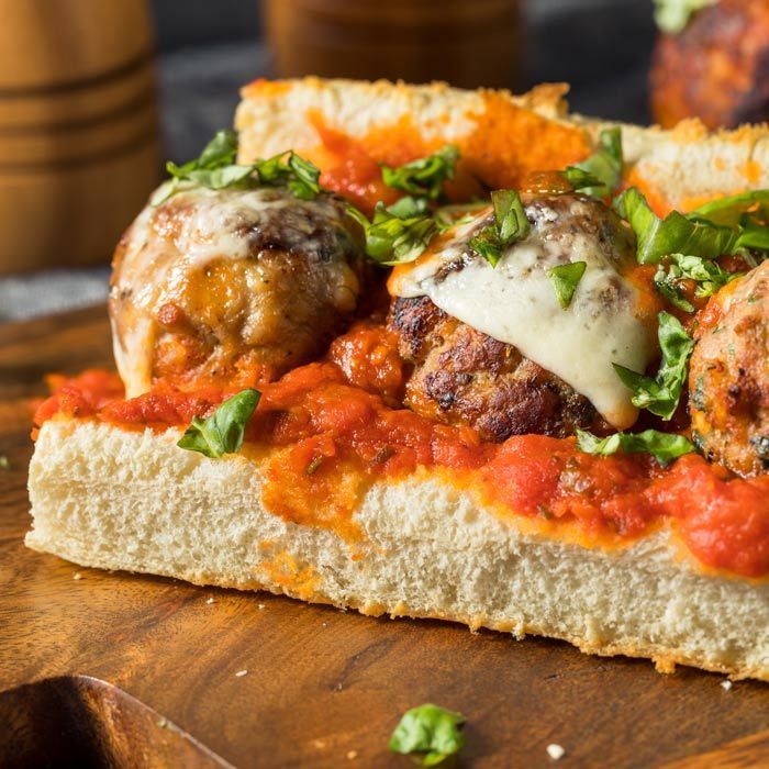 Meatballs on crusty bread with tomato sauce, melted cheese, and chopped basil on a wooden board
