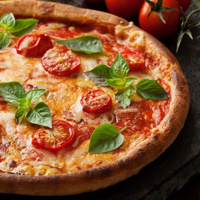Margherita pizza with cherry tomatoes and basil on a rustic wooden table