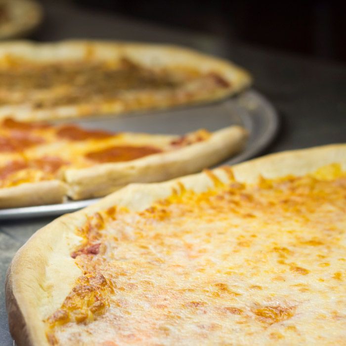 Three cheese pizzas on metal trays, with a close-up slice in the foreground