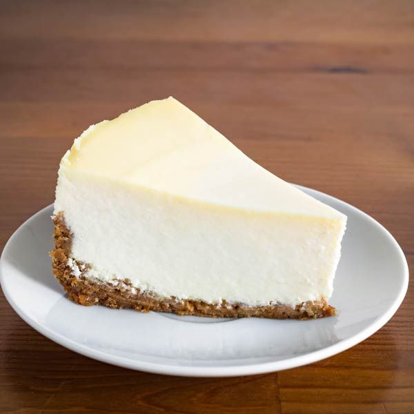 Slice of plain cheesecake on a white plate on a wooden table
