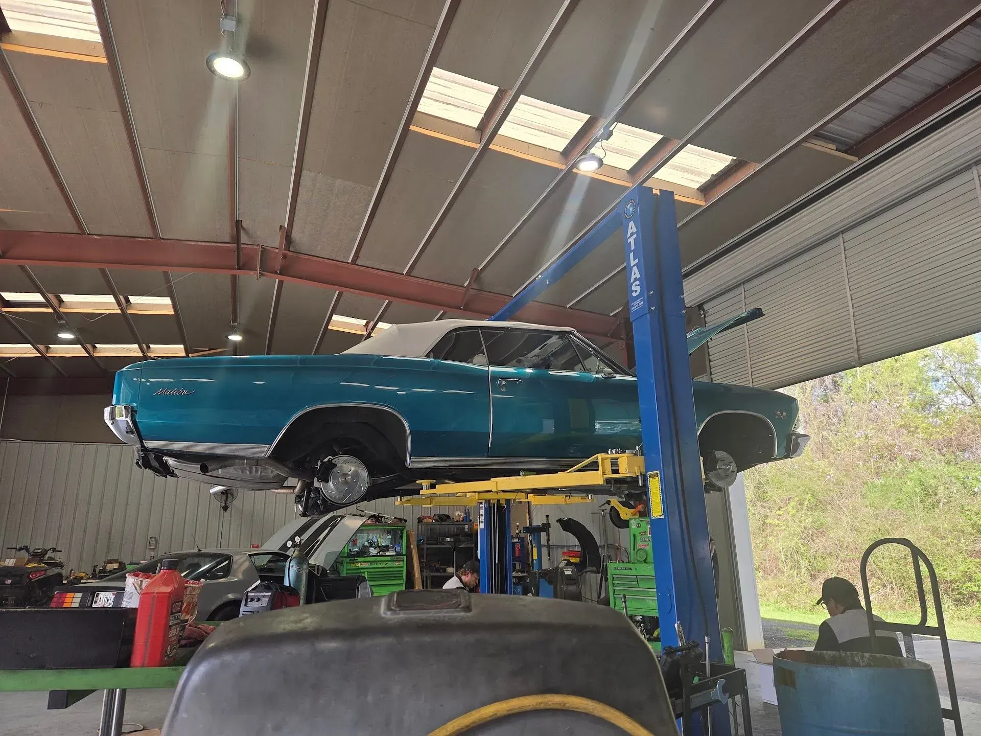 A blue classic car with a white roof on a hydraulic lift inside a garage | Hutchins Auto Repair LLC