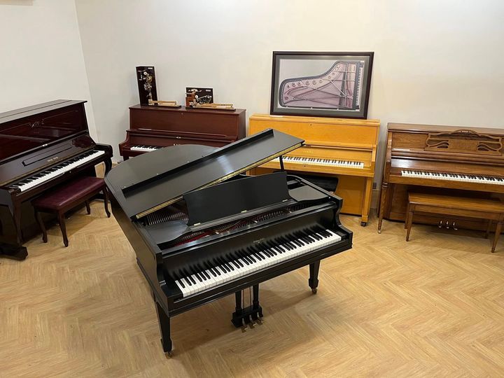 Piano showroom with several upright pianos and a black grand piano in the center.