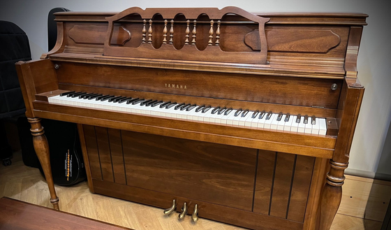 Wooden upright piano with ornate carved top and open keyboard in a room