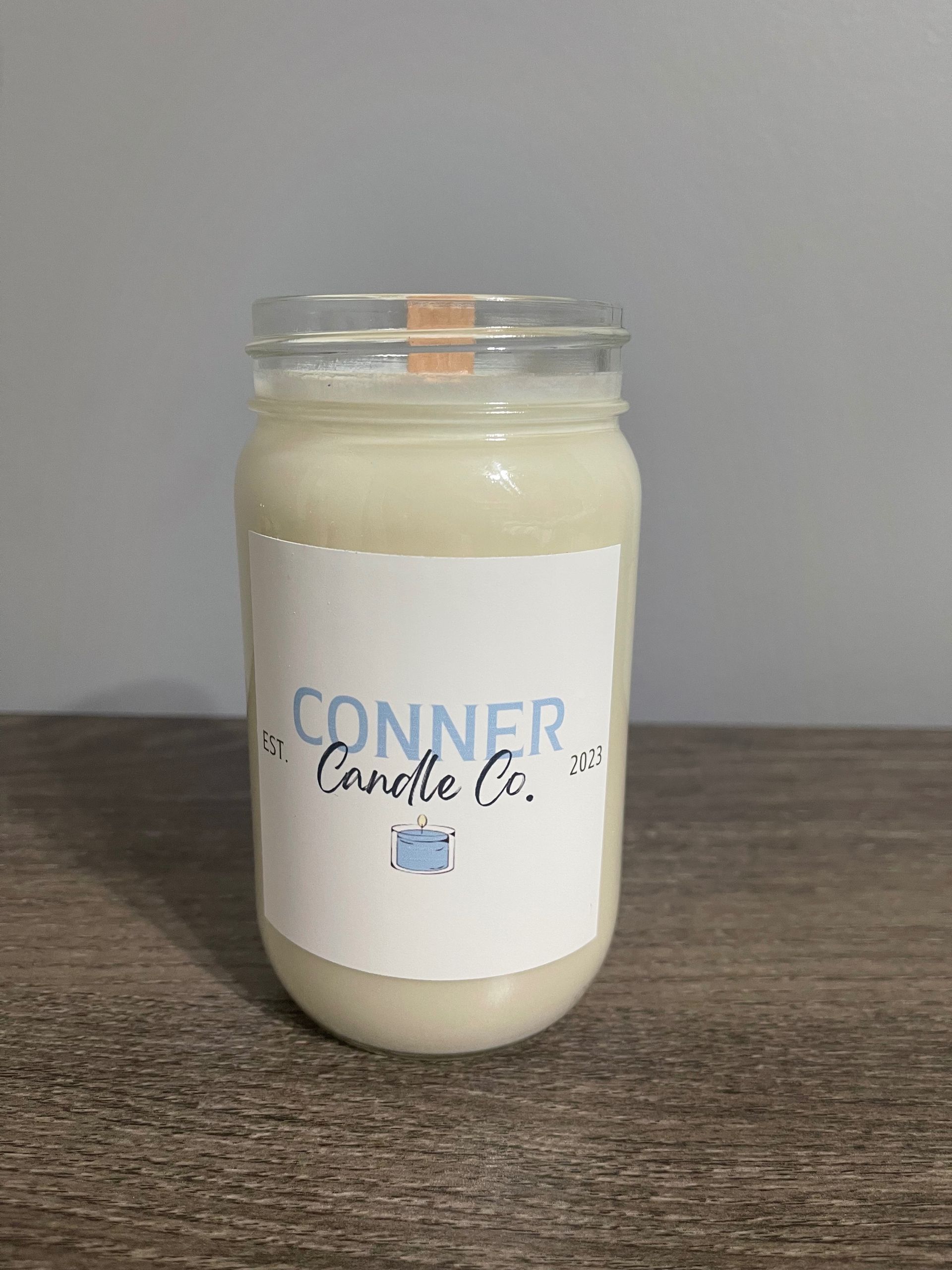 Mason jar candle with white wax, label reads "Conner Candle Co." on a wood table.