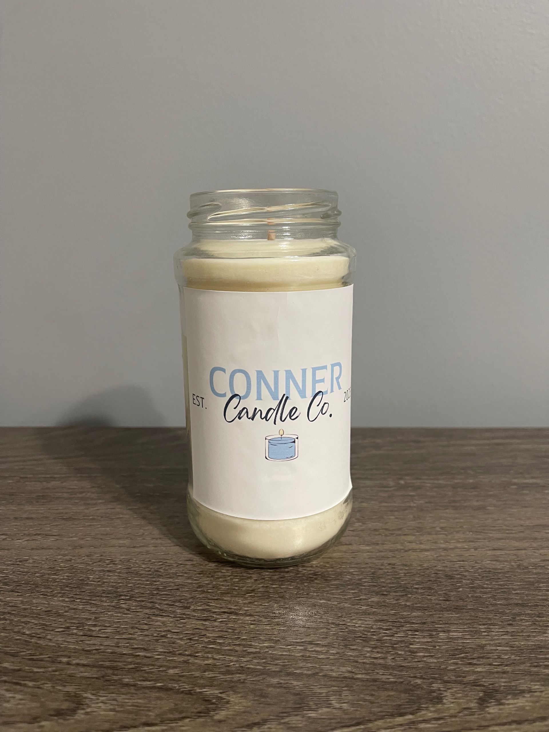 Candle in a jar with a label that says "Conner Candle Co." on a wooden surface.