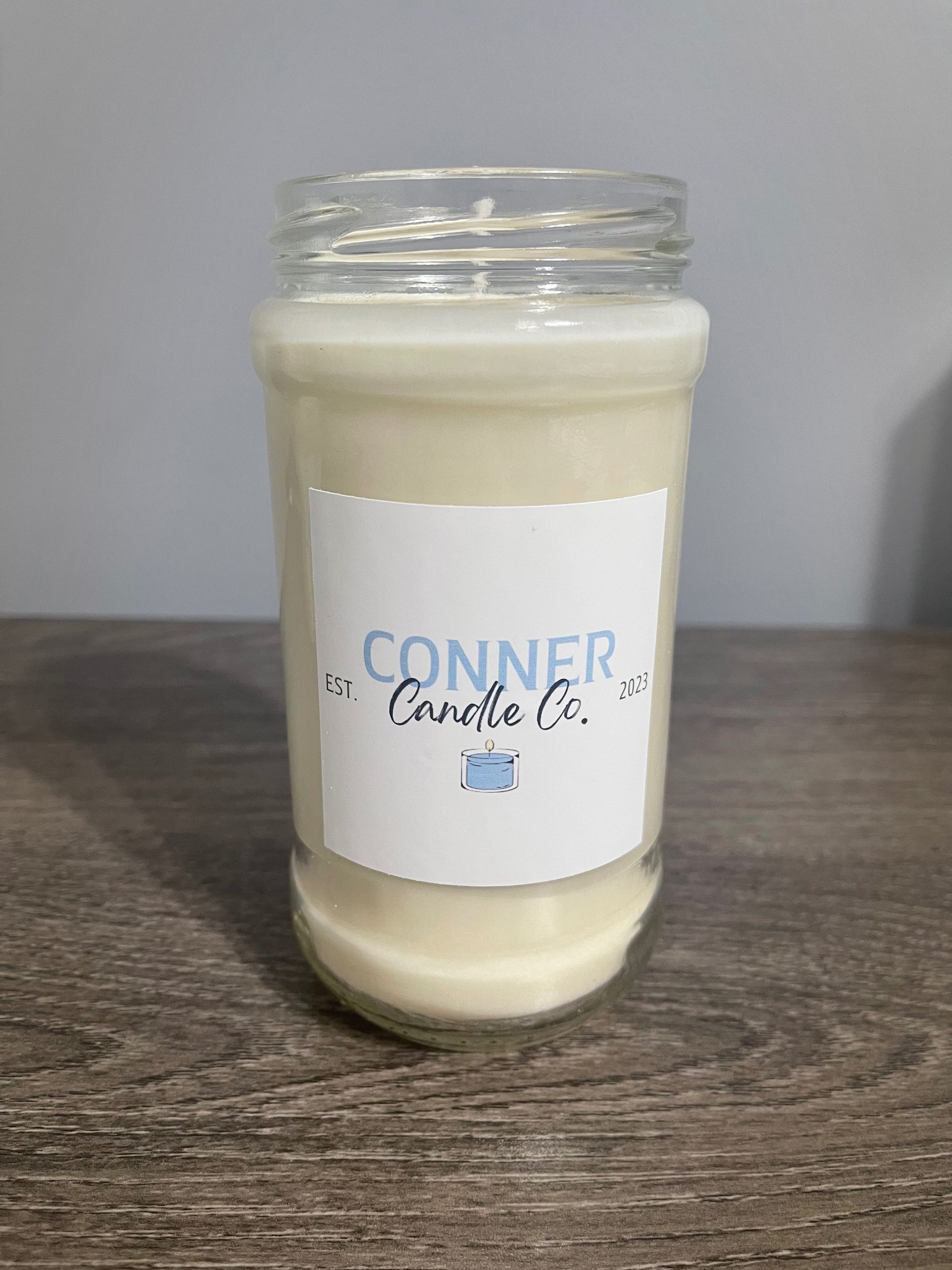 Glass jar candle with white wax, a "Conner Candle Co." label, set on a wood surface.