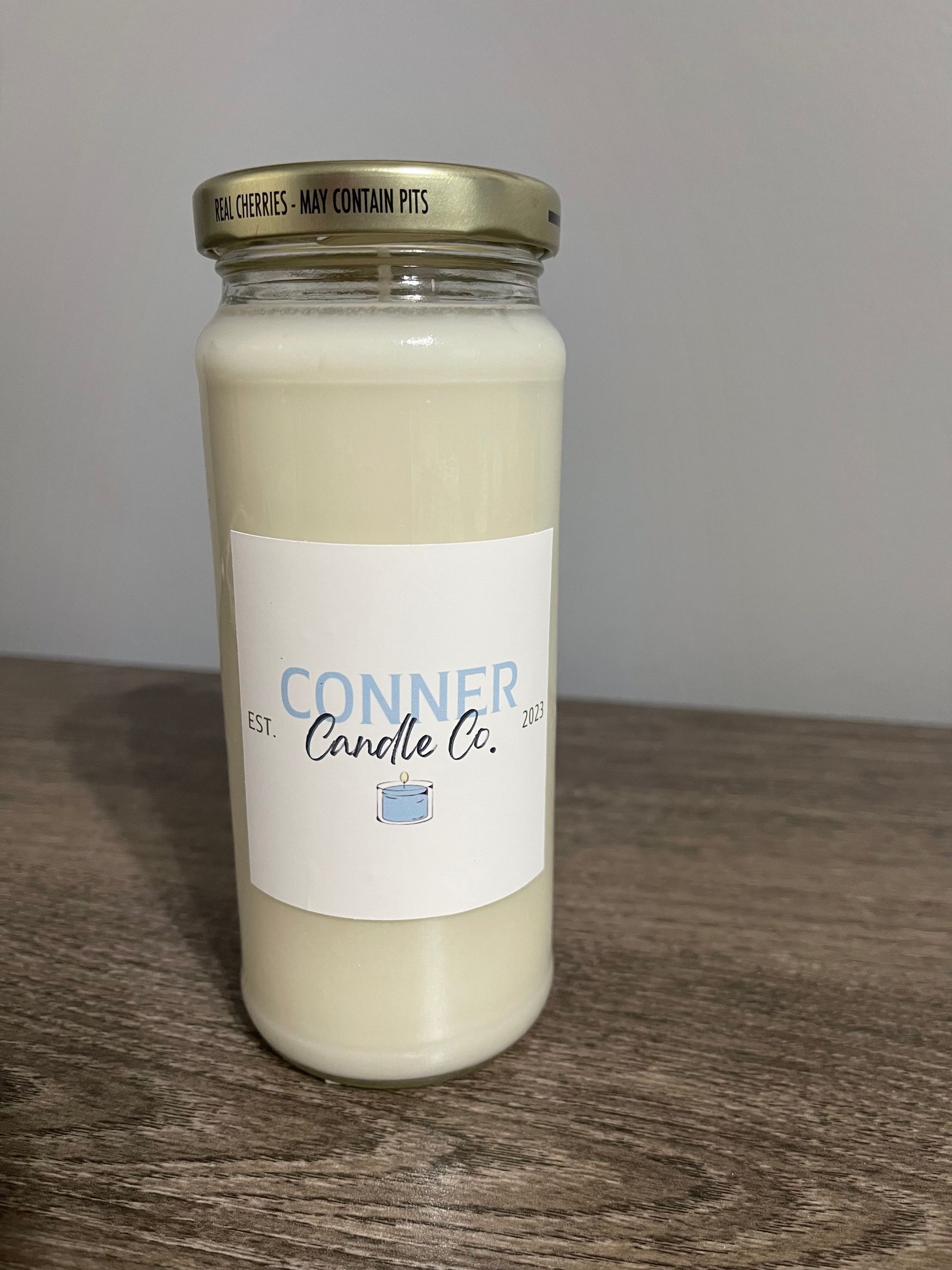 Candle in a jar with label "Conner the Candle Co." on a wooden surface.