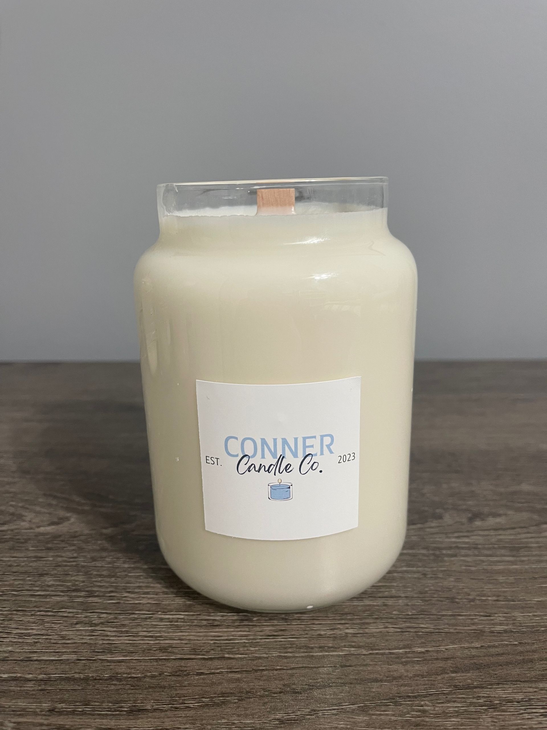 White candle in a jar with "Conner Candles" label, sitting on a wooden surface.
