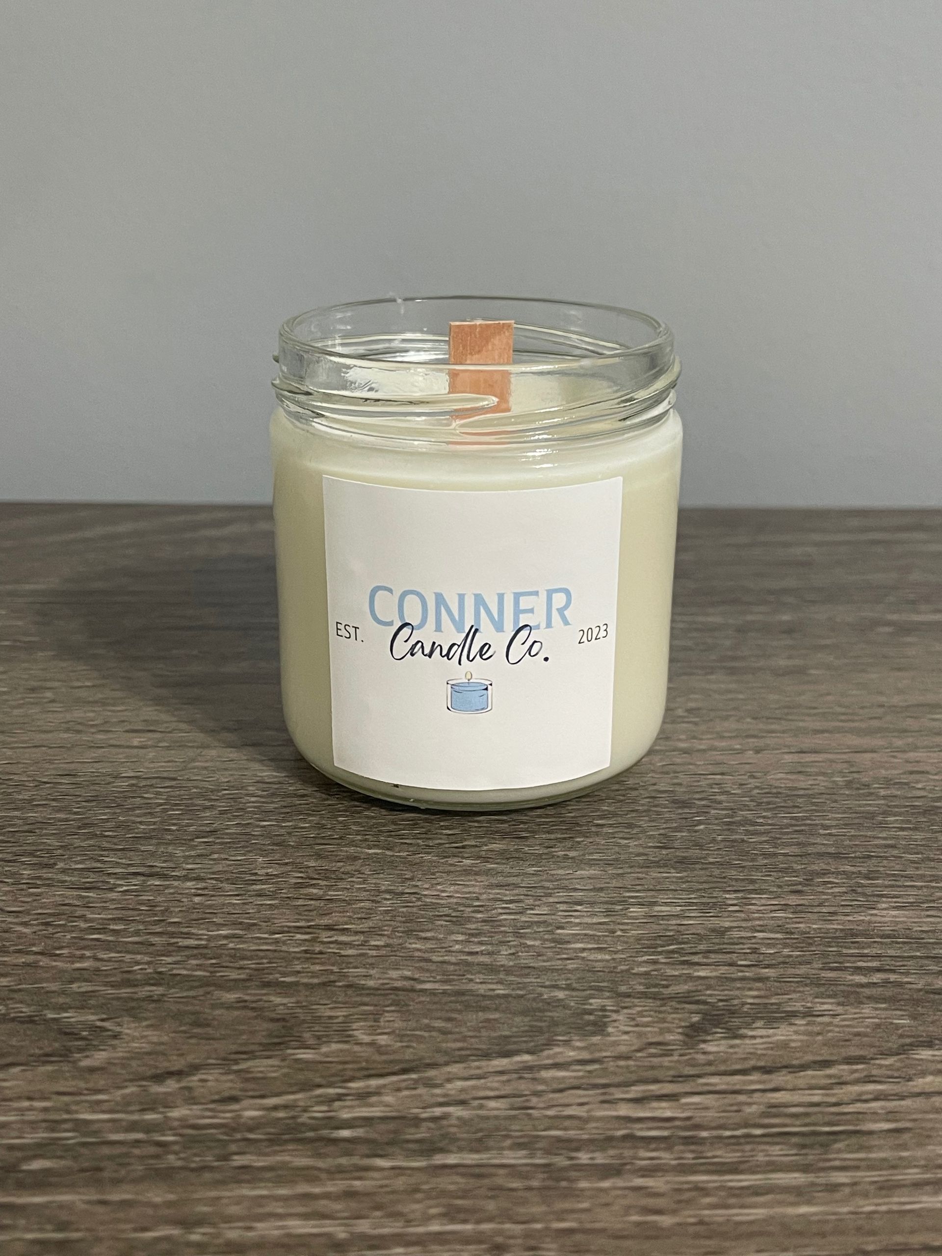 Candle in a jar with a label that says "Conner Candle Co." on a wooden table.