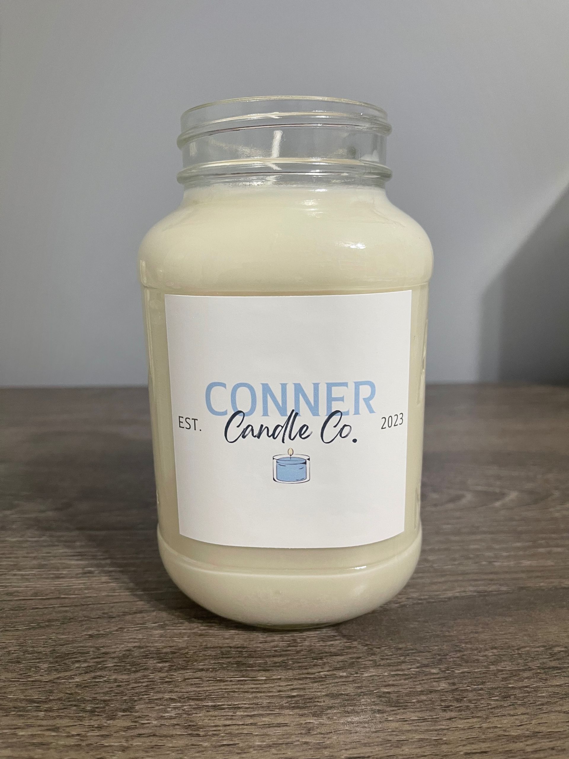 Candle in a jar with label "Conner Candle Co." on a wooden surface.