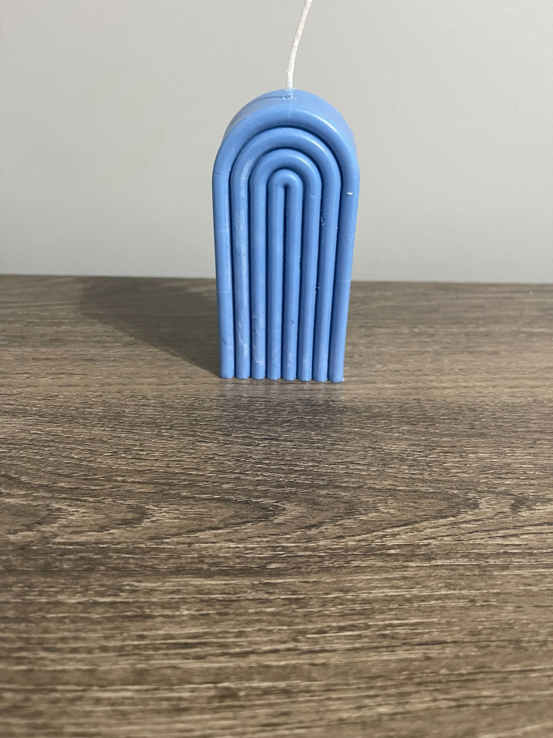 Yellow candle in a curved, arch design on a wooden surface.