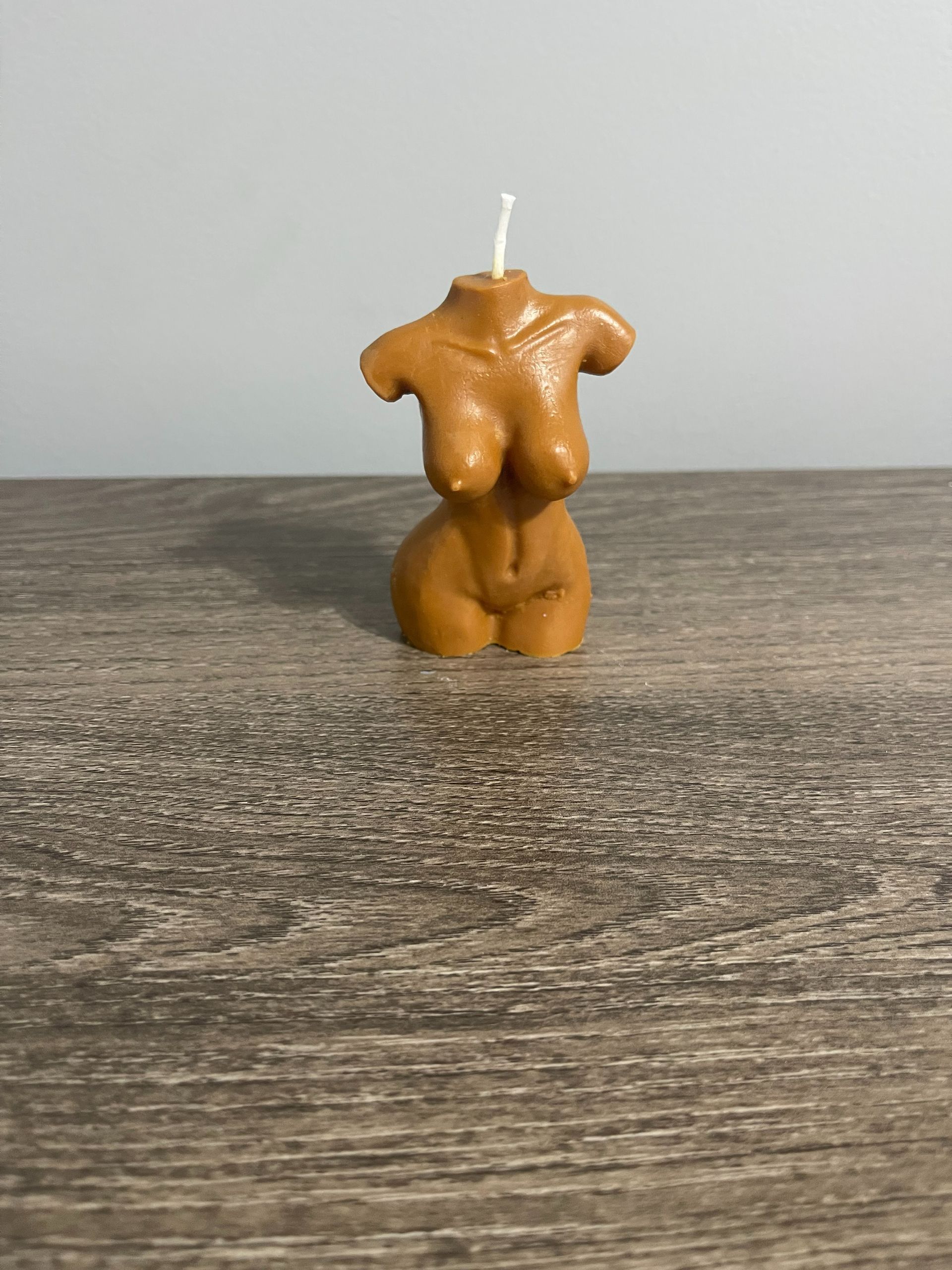 Cream-colored, torso-shaped candle with a wick, sitting on a wooden surface.
