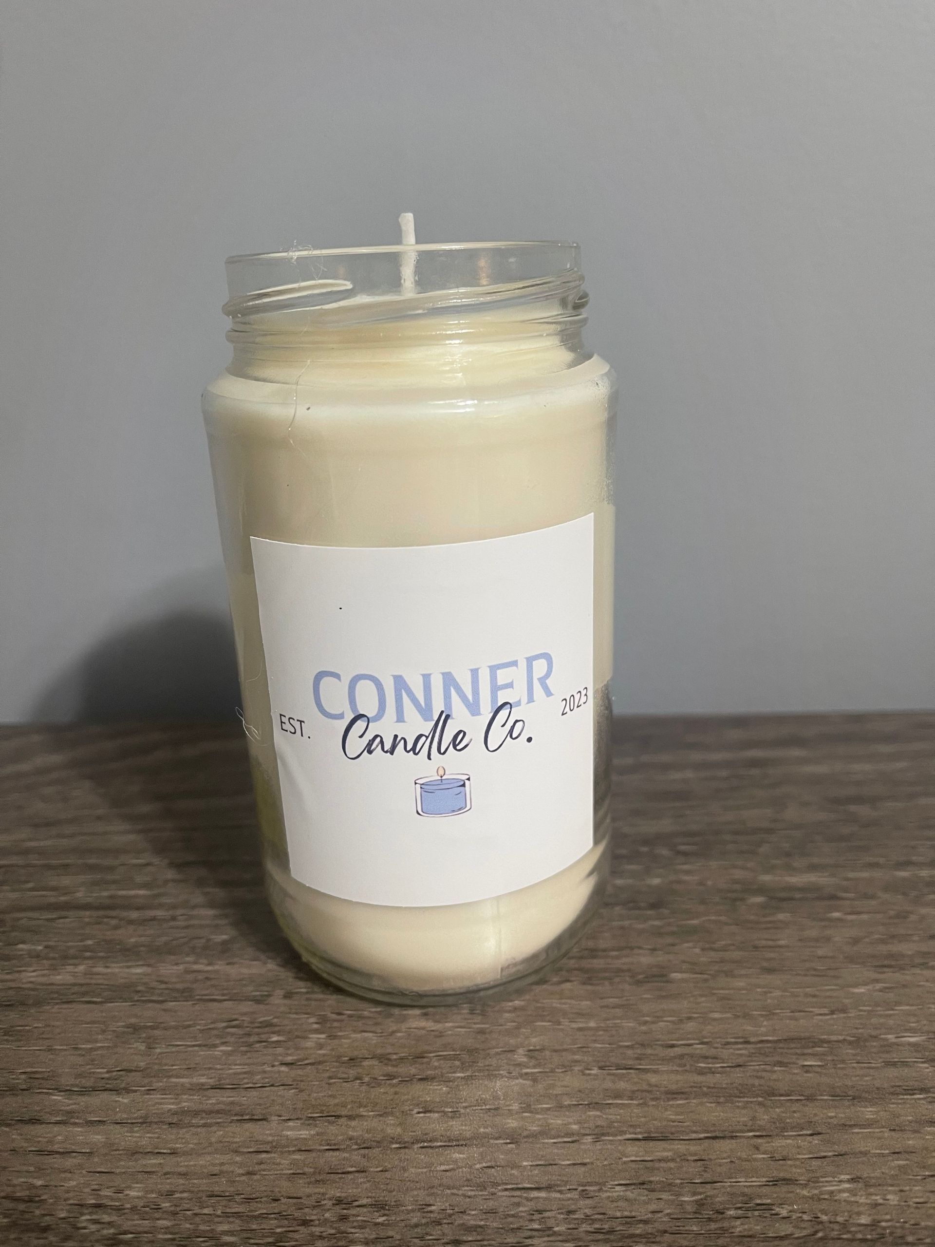 Cream-colored candle in a clear glass jar with a white label reading "Conner Candle Co." on a wooden surface.