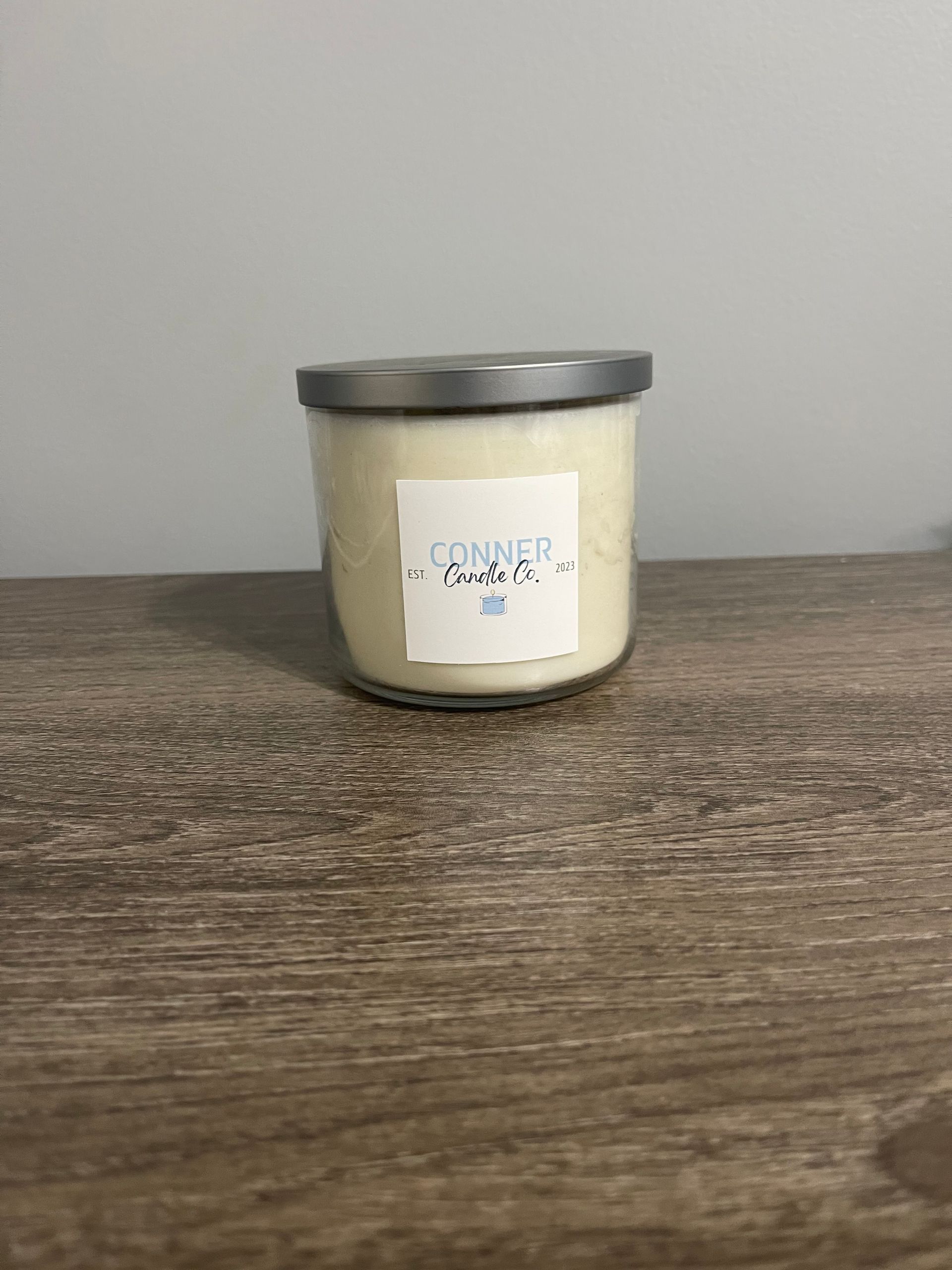 Candle in a glass jar with a silver lid on a wood surface; label reads "powder".