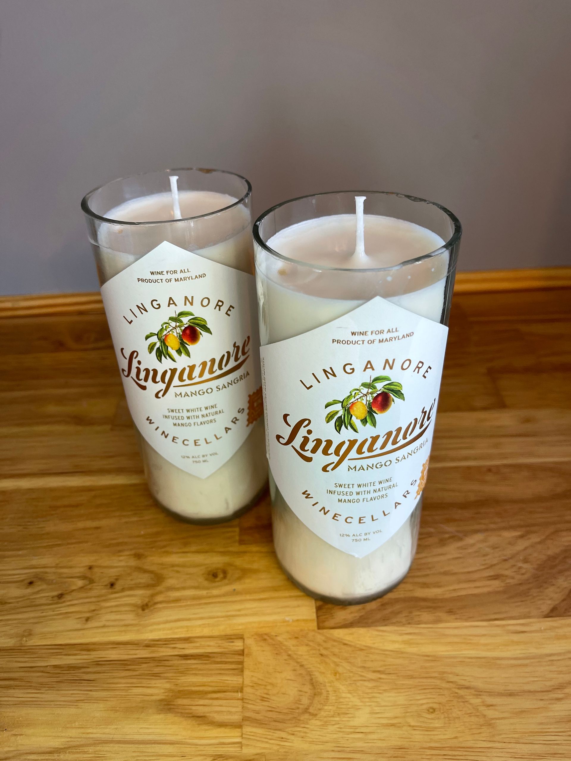Two clear tumblers with white candles and gold “Linganore” labels on a wooden table