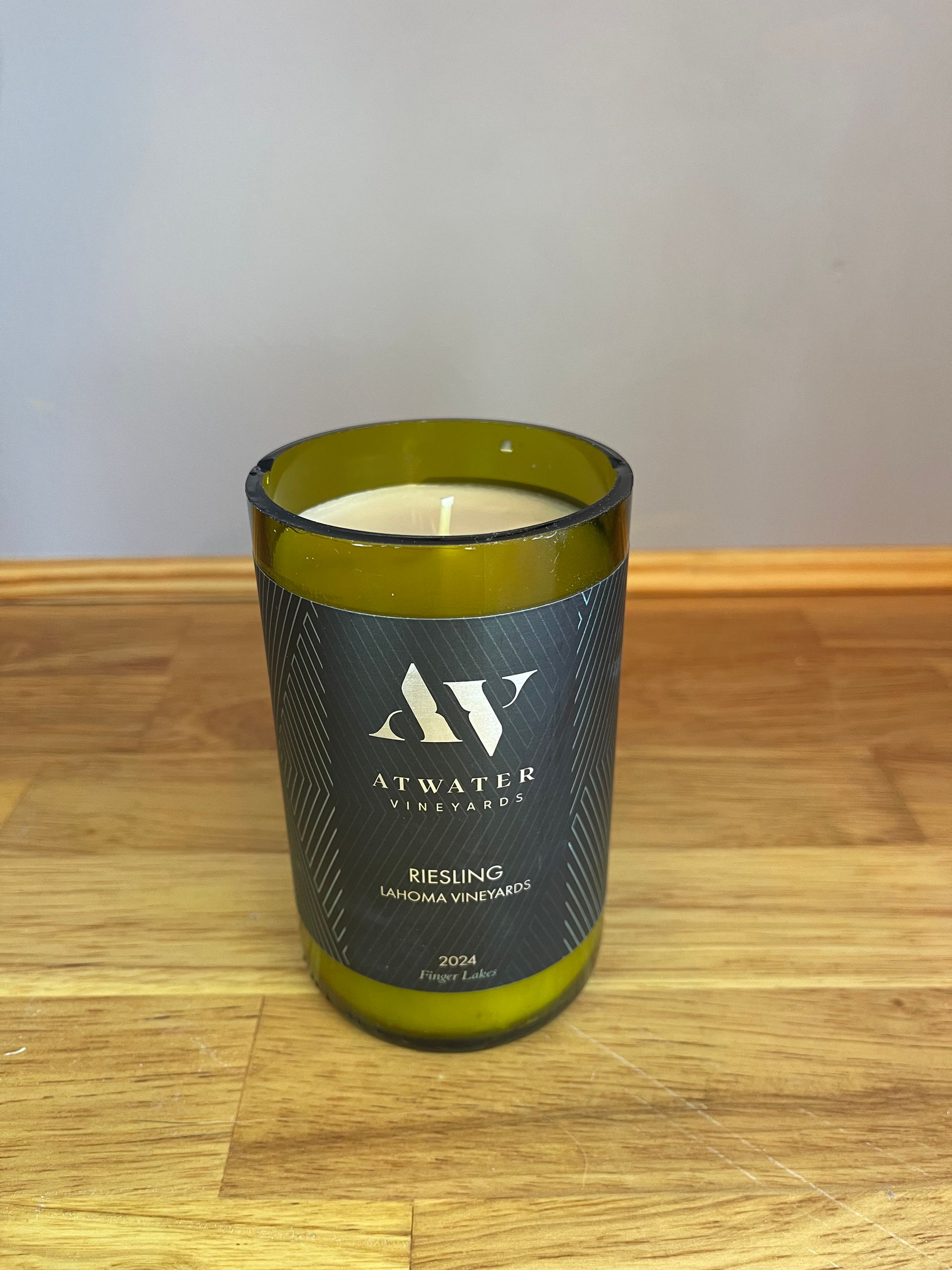 Green glass candle on a wooden table against a gray wall.