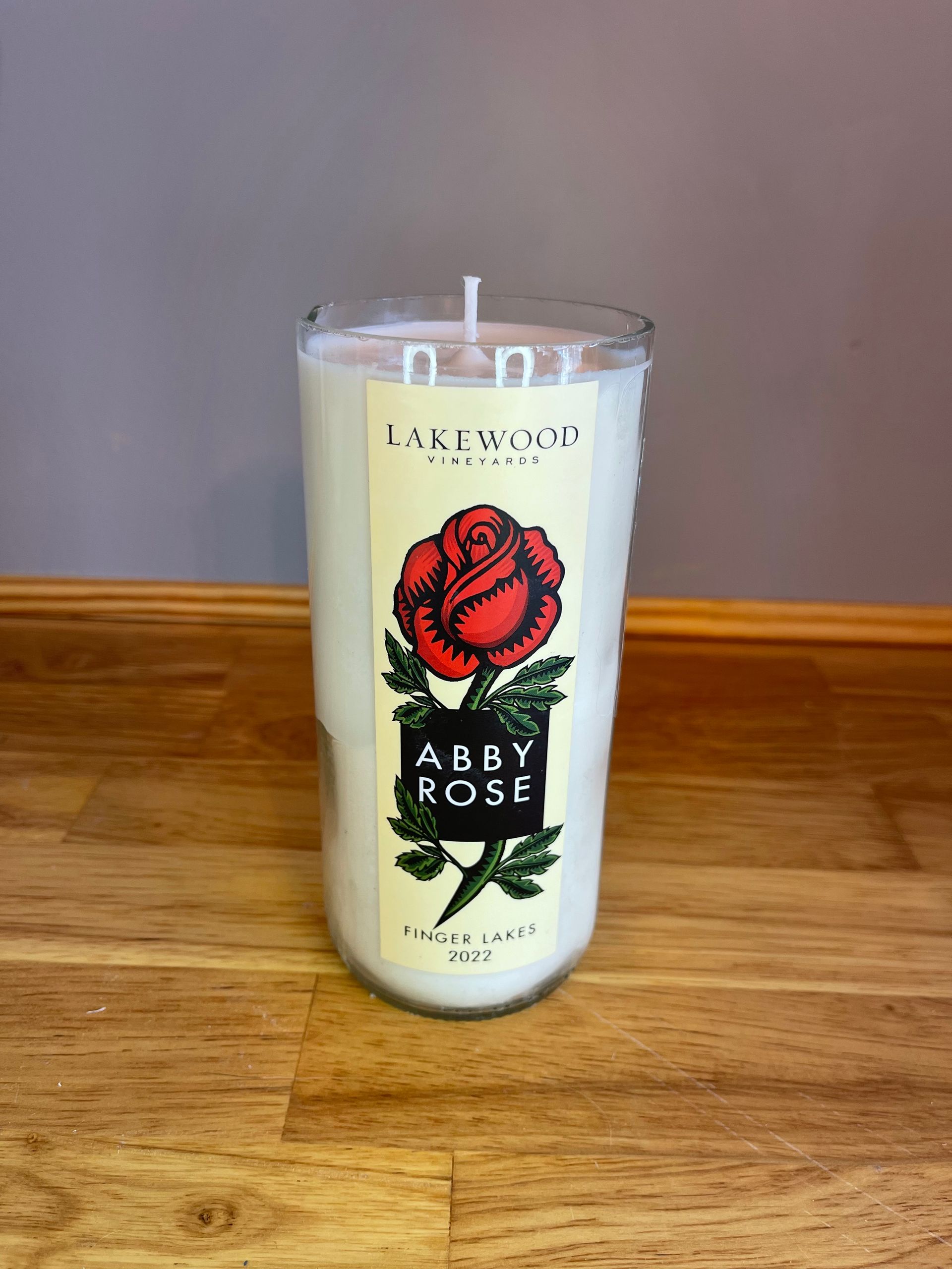 Lit candle in a clear glass with red rose and “ABBY ROSE” label on a wooden table