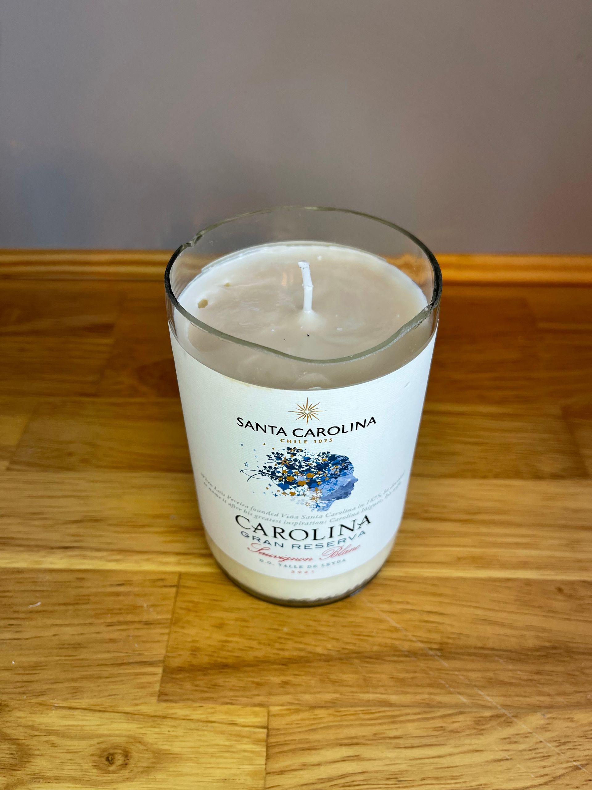 White Carolina Inn candle jar on a wooden table against a wood floor background