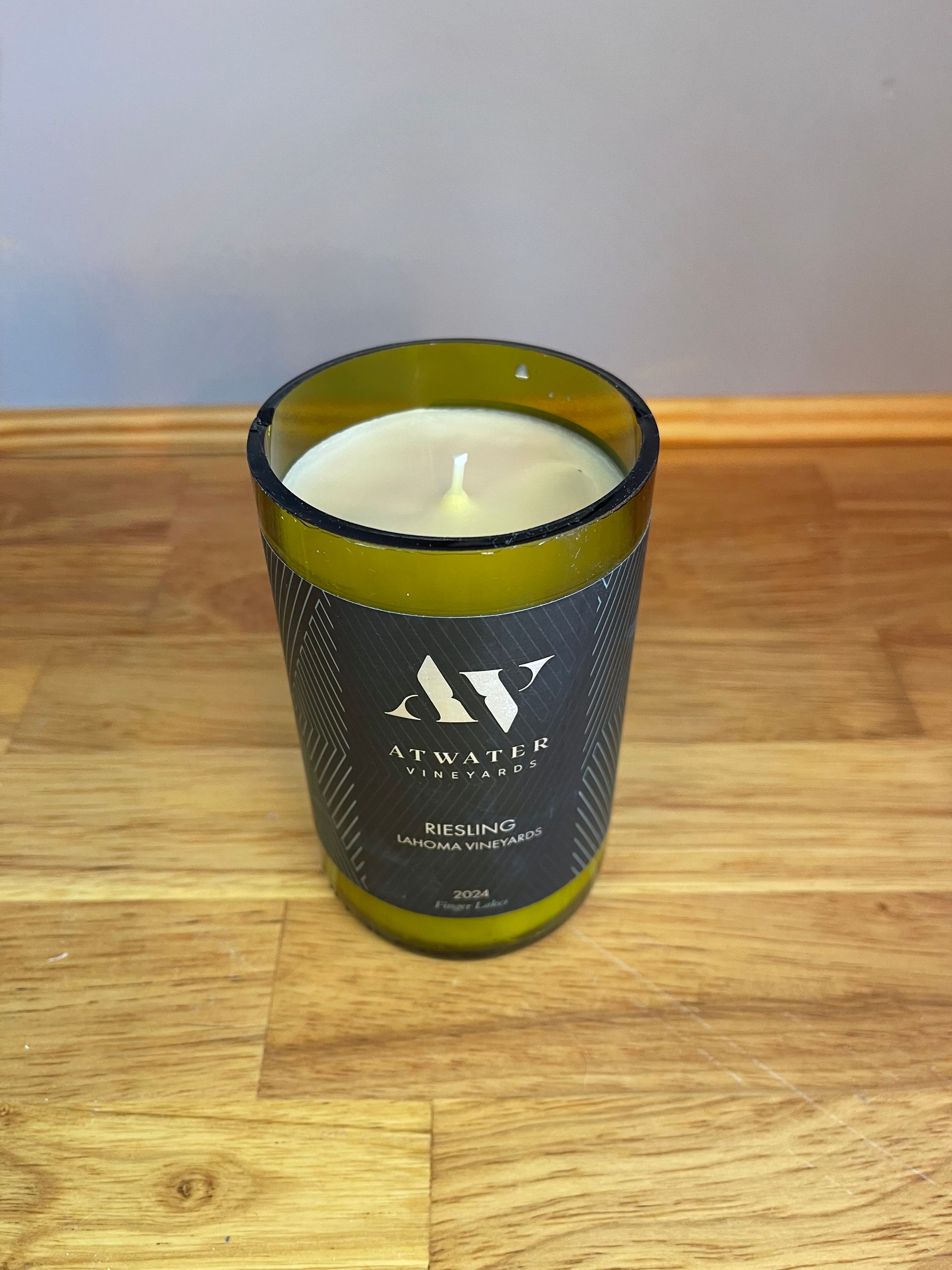 Green glass candle on a wooden table against a gray wall.