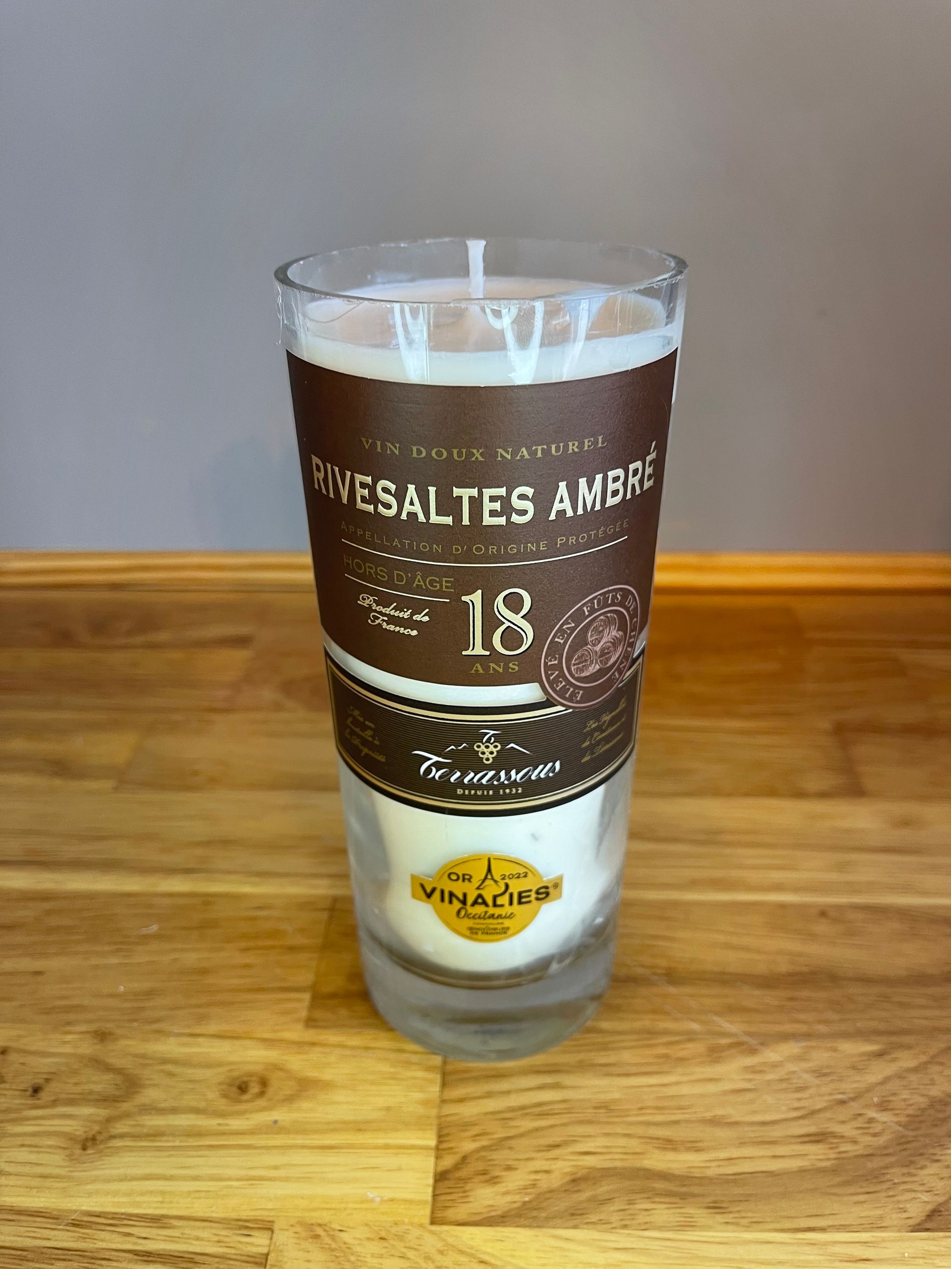 Clear shot glass with brown label and gold text on a wooden table against a gray background
